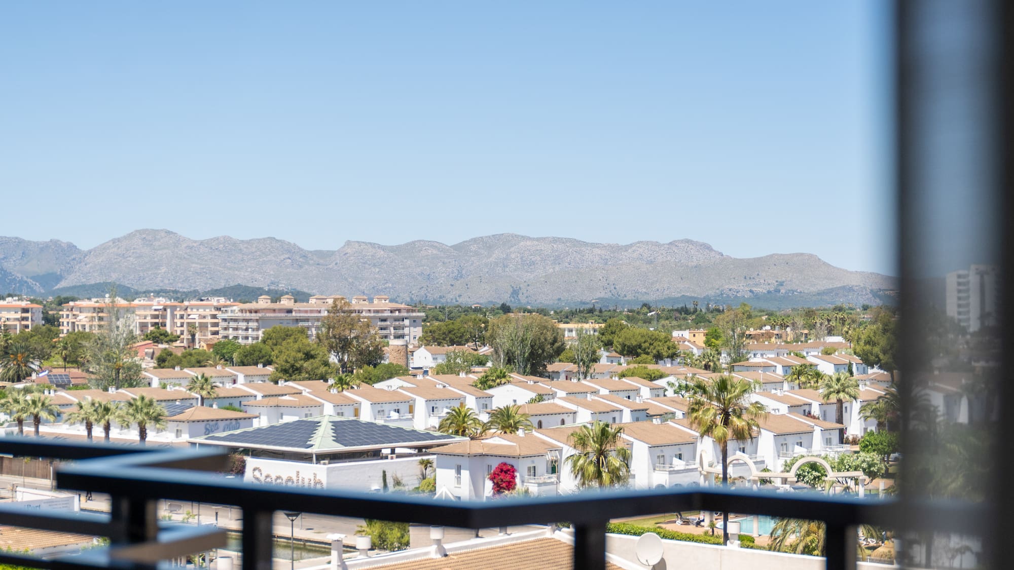 Elevated view of white villas, palm trees, and mountains against a clear sky.
