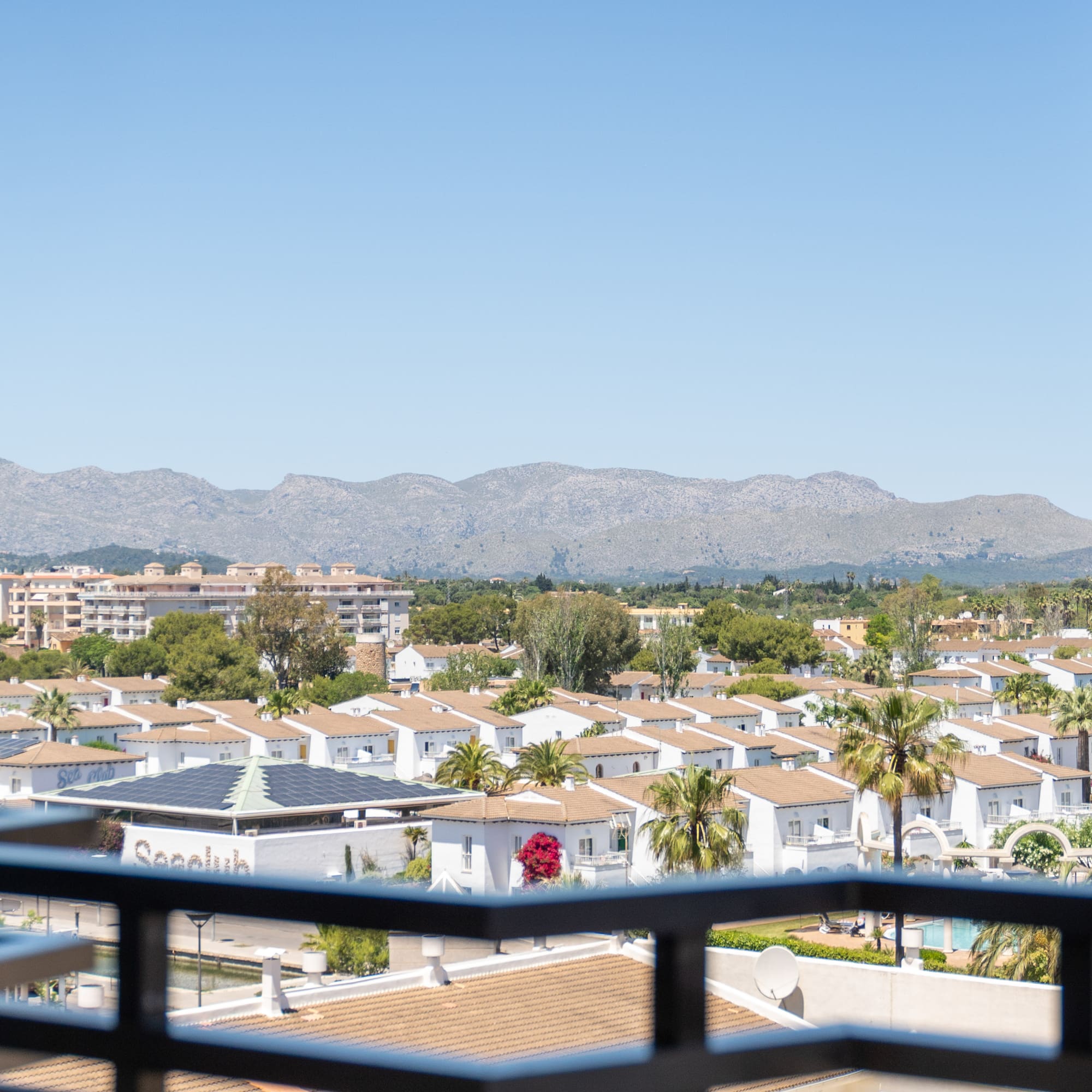 Elevated view of white villas, palm trees, and mountains against a clear sky.