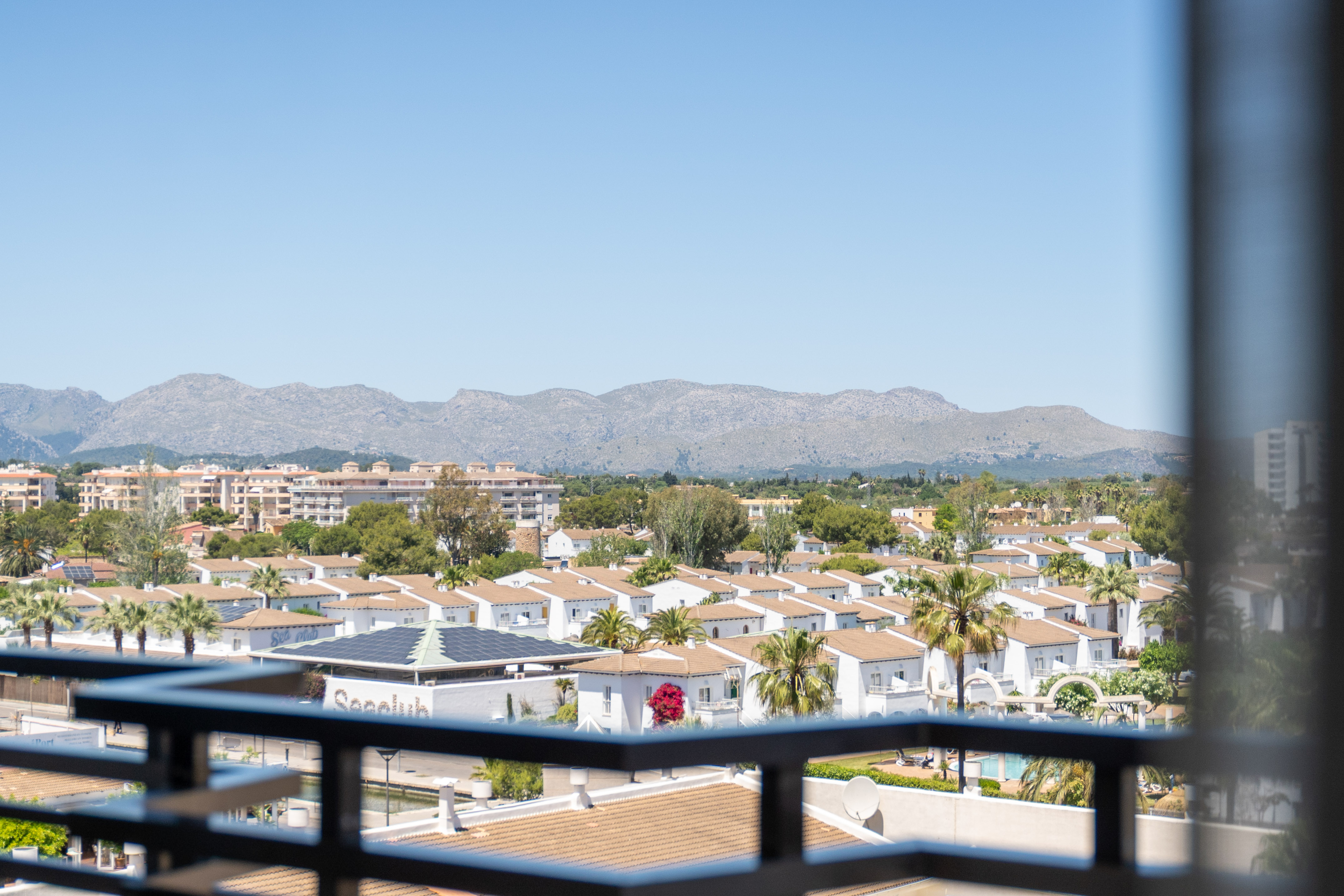 Elevated view of white villas, palm trees, and mountains against a clear sky.