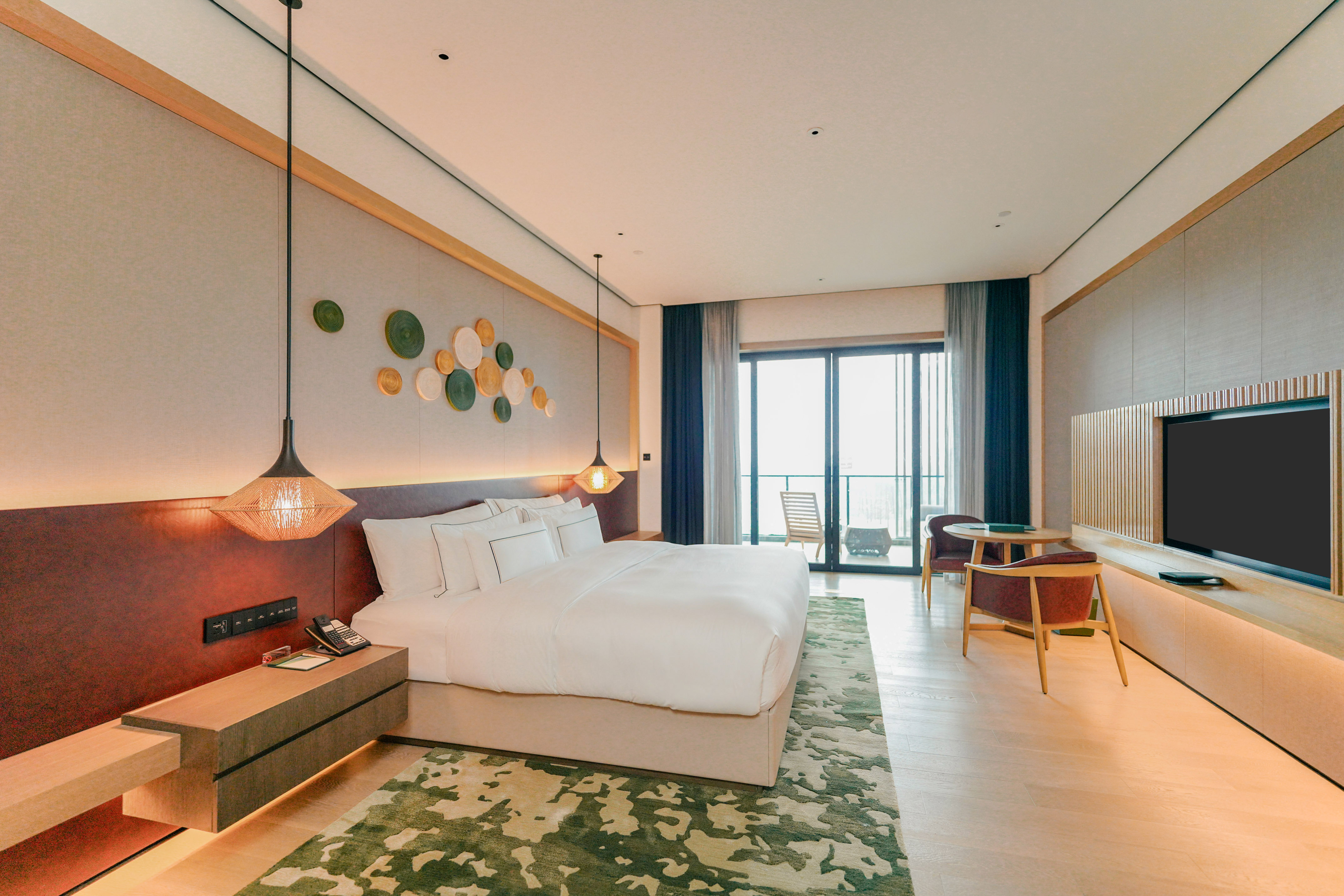 Modern hotel suite with king bed, balcony, abstract rug, and TV.