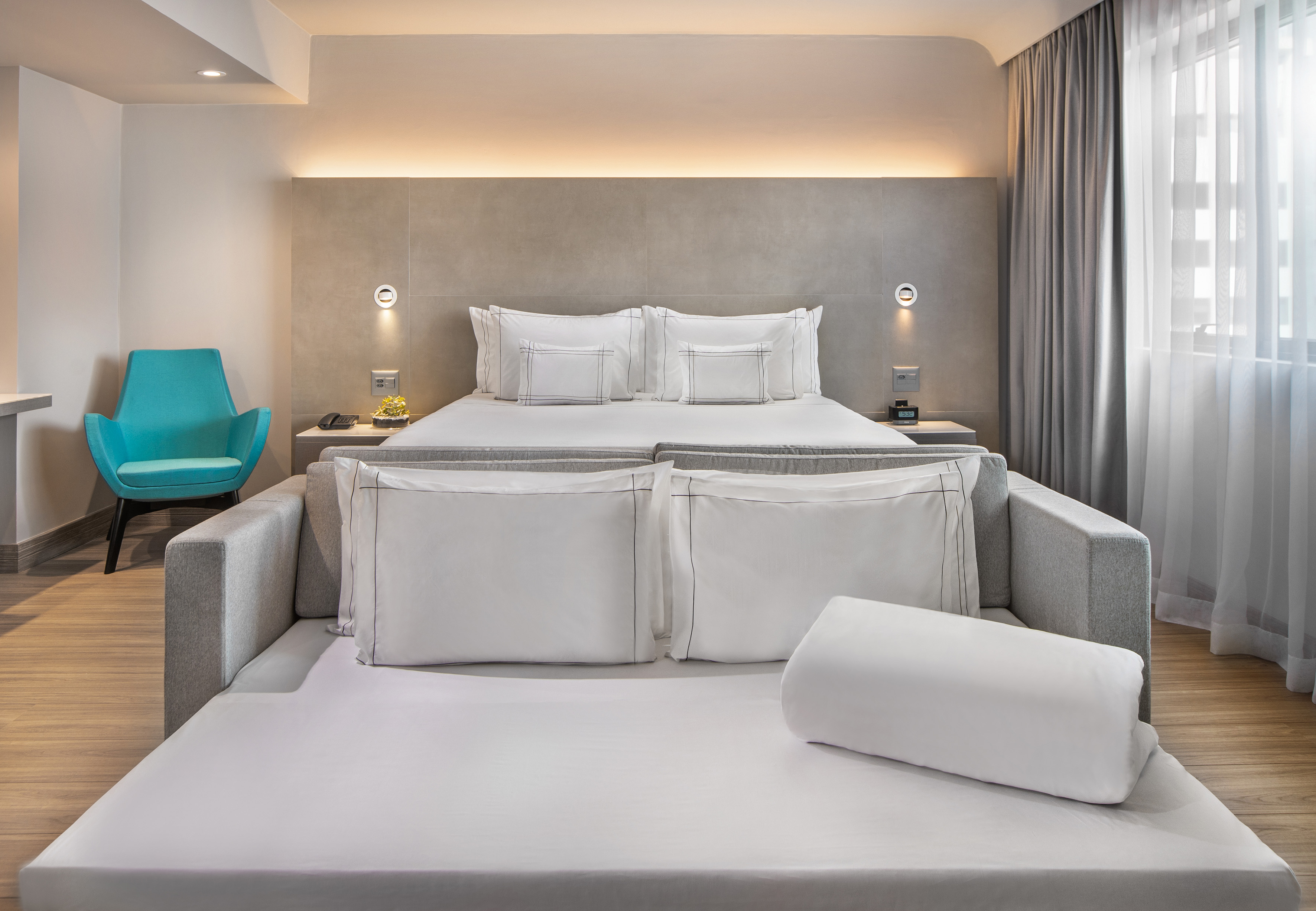Contemporary hotel room featuring a king bed, sofa bed, and vibrant blue chair.