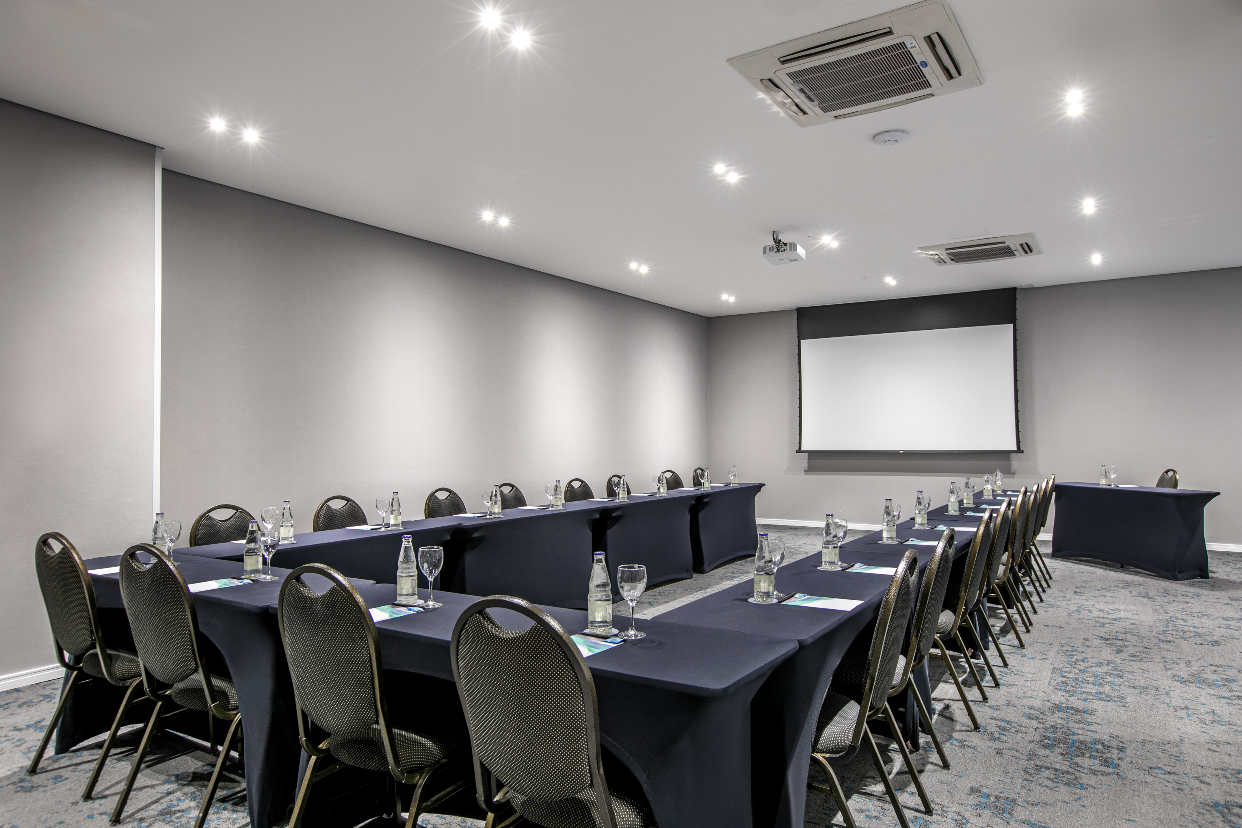 Modern conference room U-shaped table setup with projector screen.