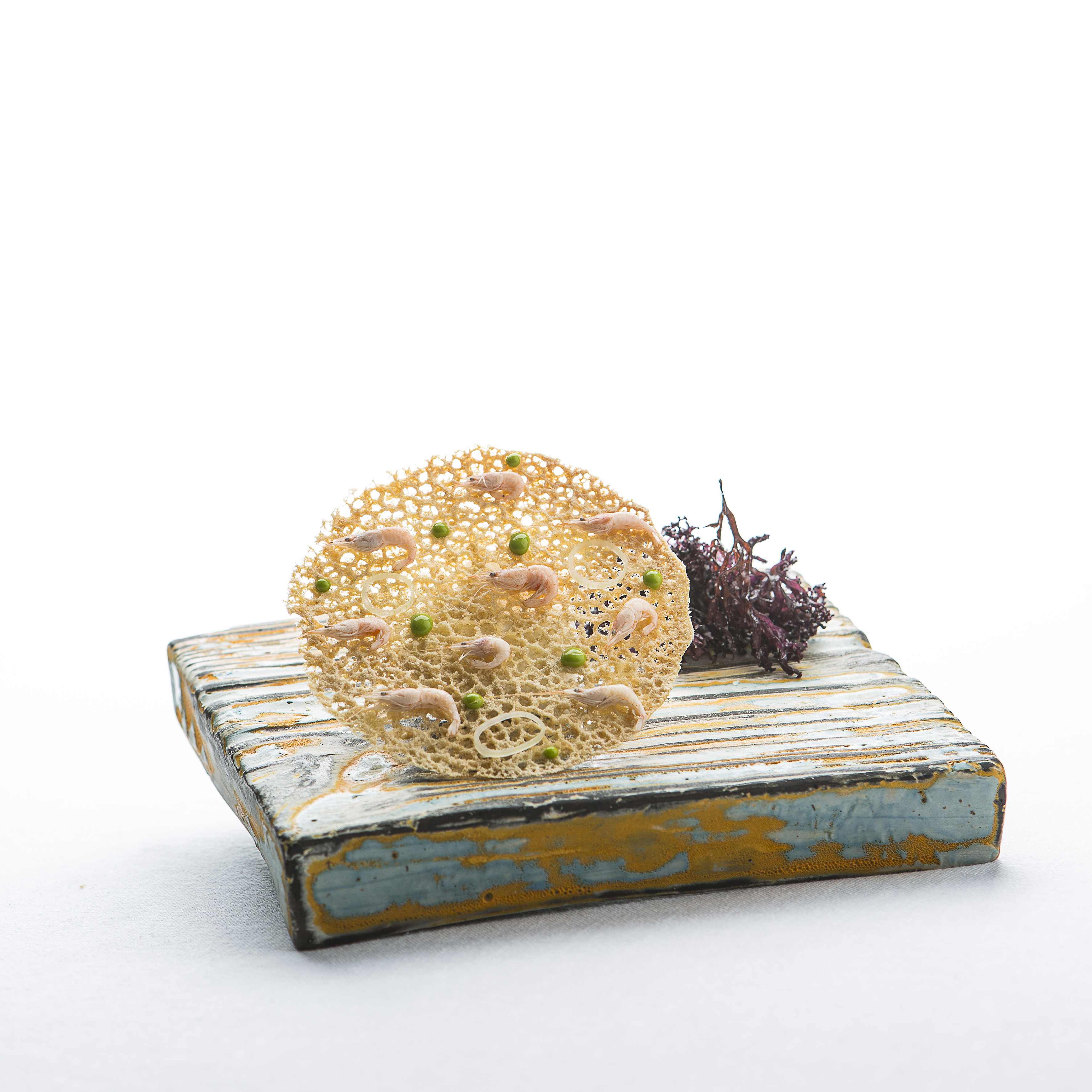 Gourmet shrimp cracker with peas, onion, and red seaweed on rustic wood.