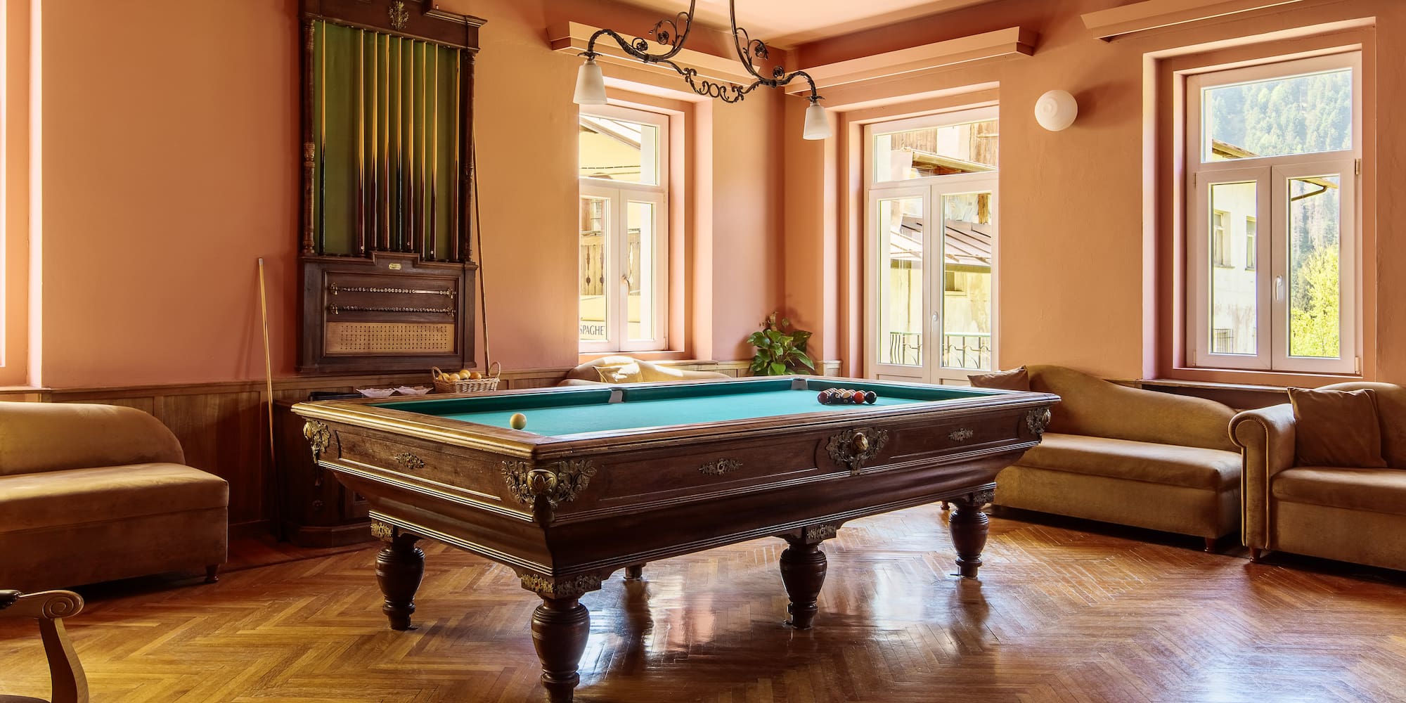 Ornate wooden billiard table with green felt and parquet floor in game room.
