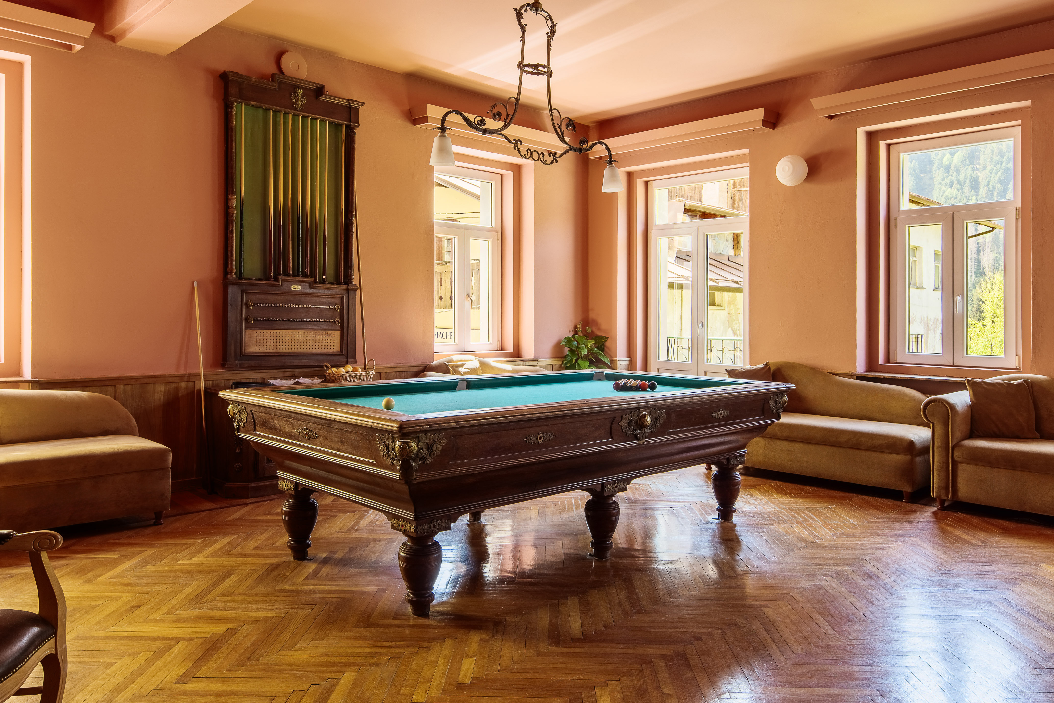 Ornate wooden billiard table with green felt and parquet floor in game room.