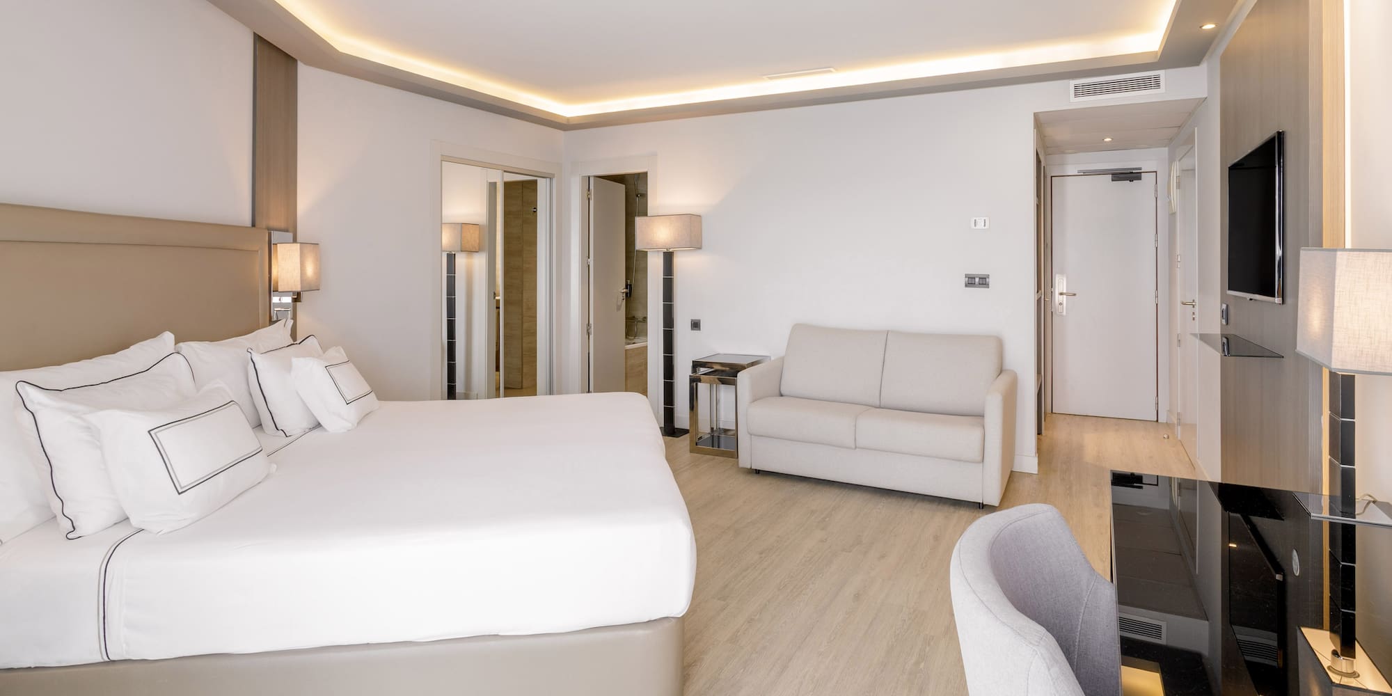 Habitación de hotel moderna con cama doble, sofá, escritorio y suelo de madera.