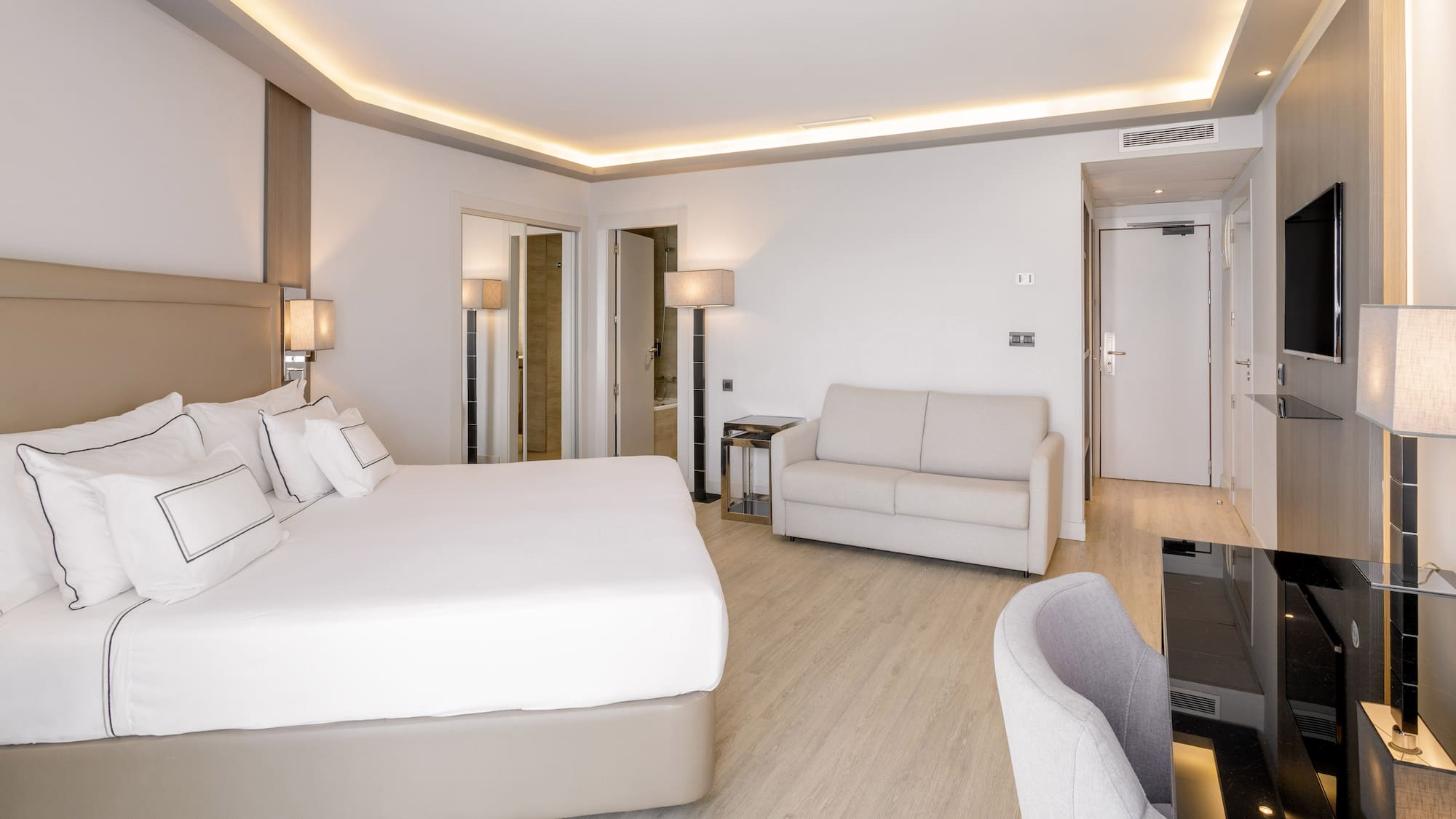 Habitación de hotel moderna con cama doble, sofá, escritorio y suelo de madera.