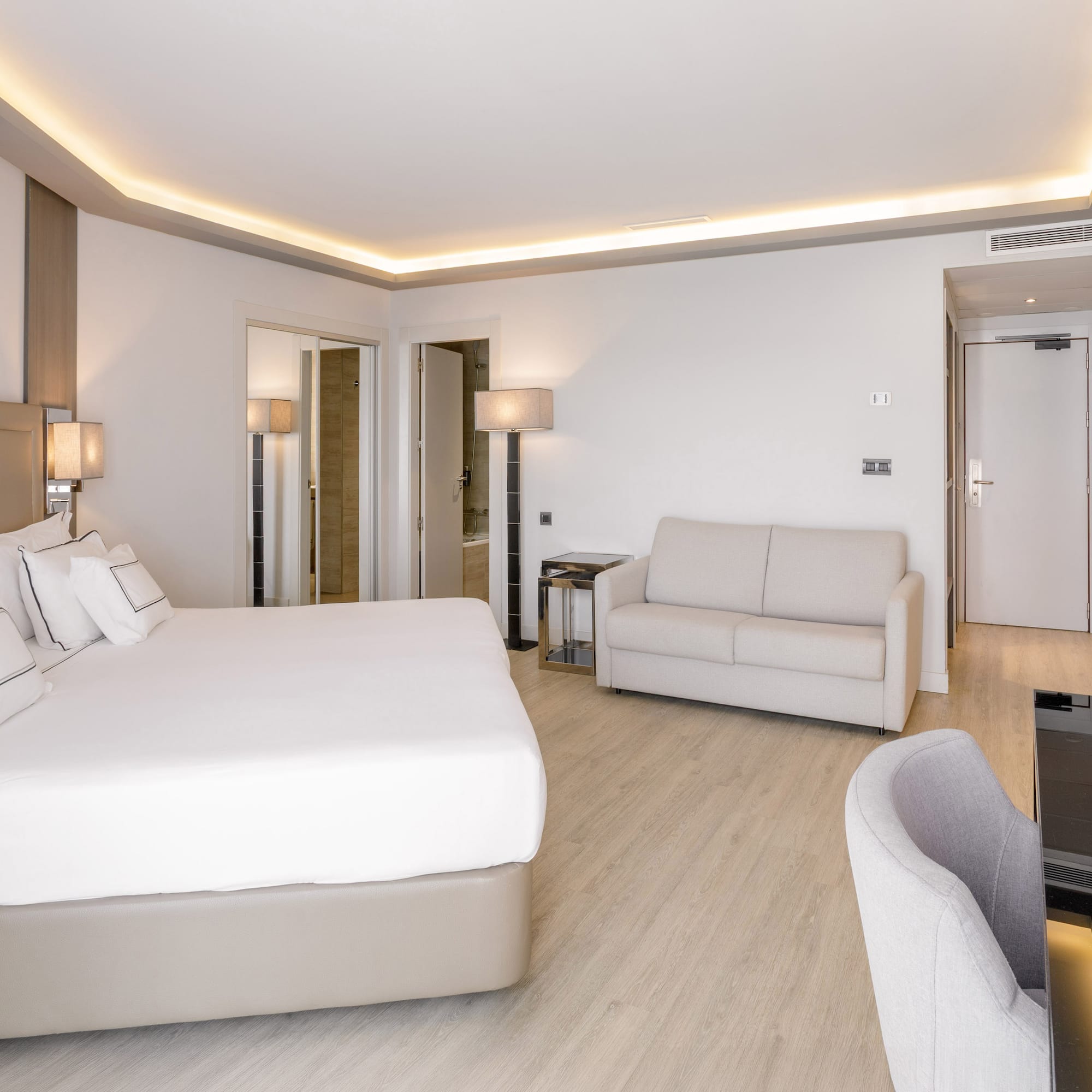 Habitación de hotel moderna con cama doble, sofá, escritorio y suelo de madera.