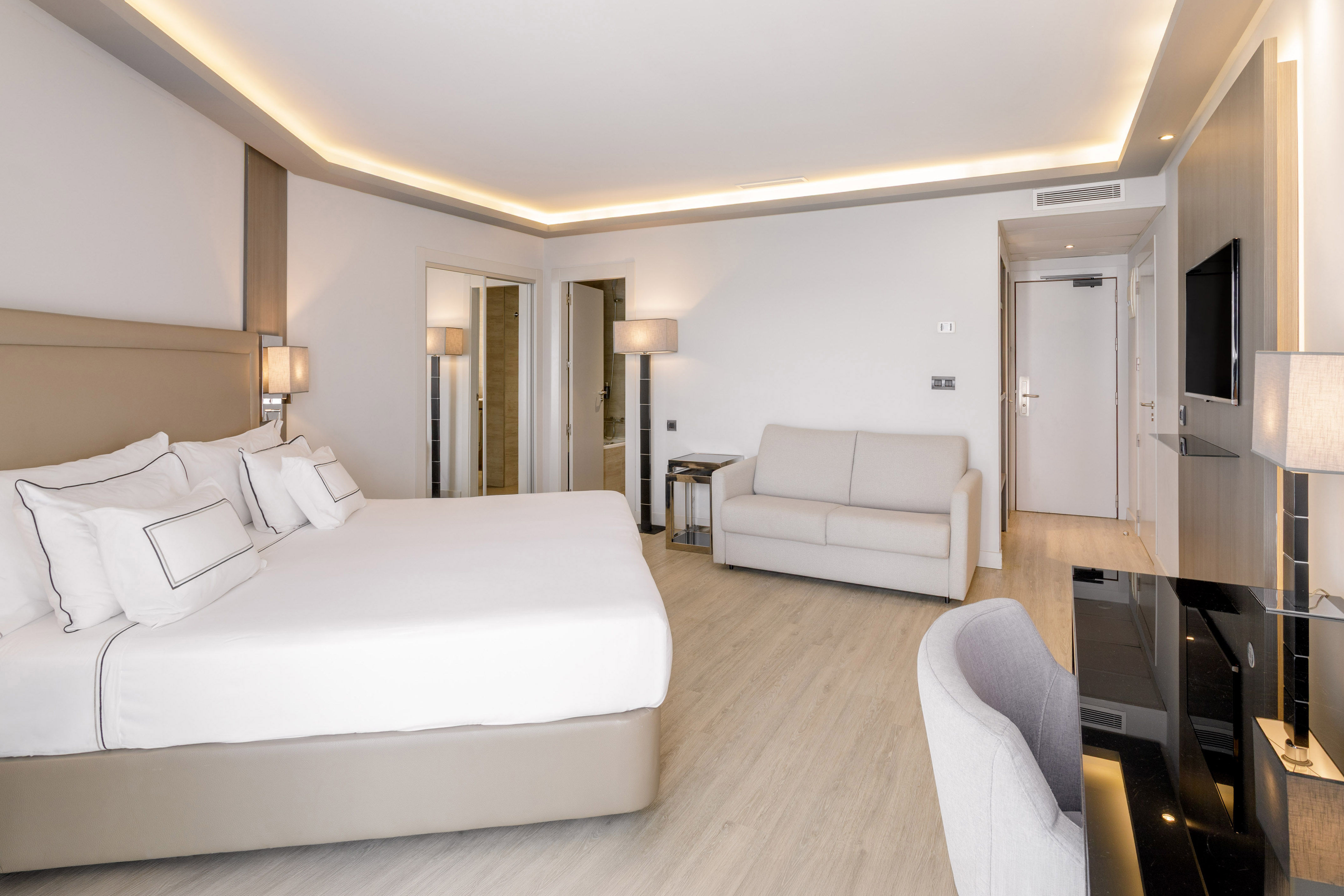 Habitación de hotel moderna con cama doble, sofá, escritorio y suelo de madera.