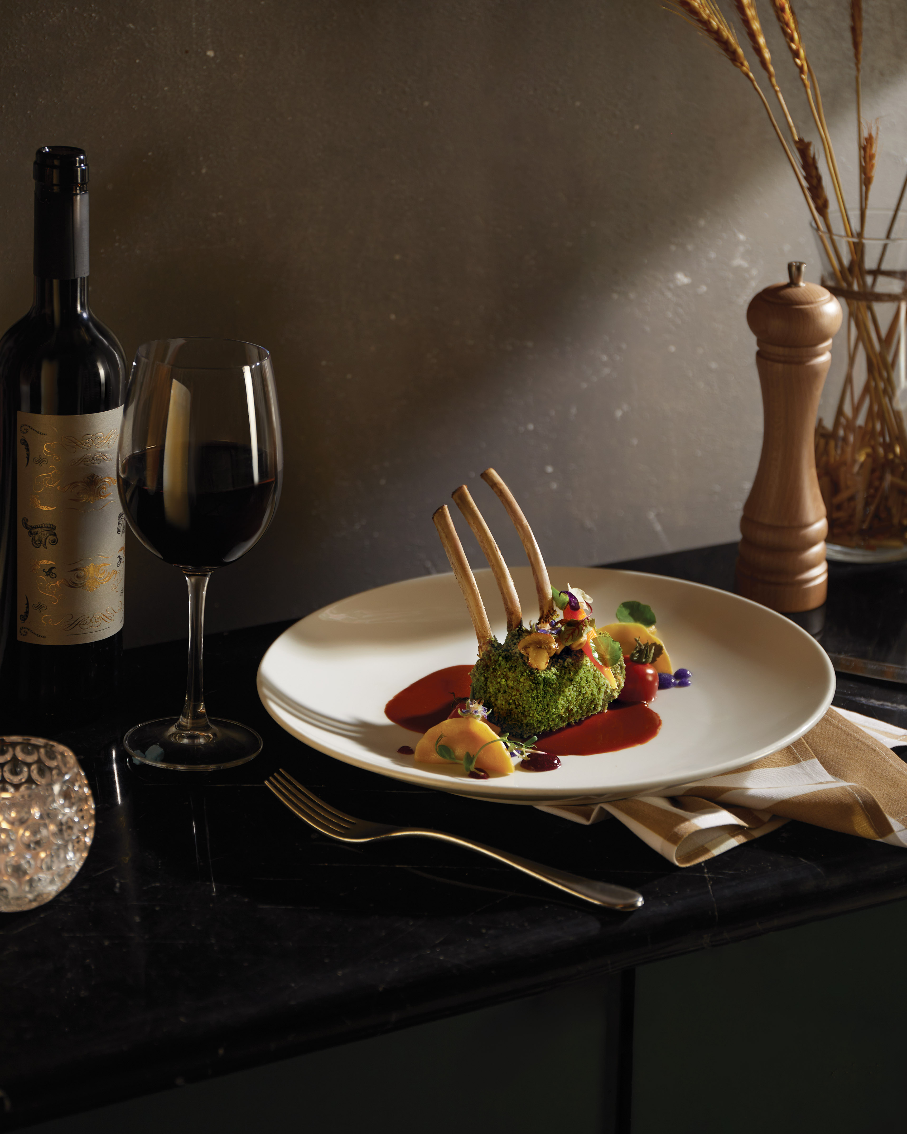Herb-crusted lamb chops, red wine, fork on an elegant dining table.