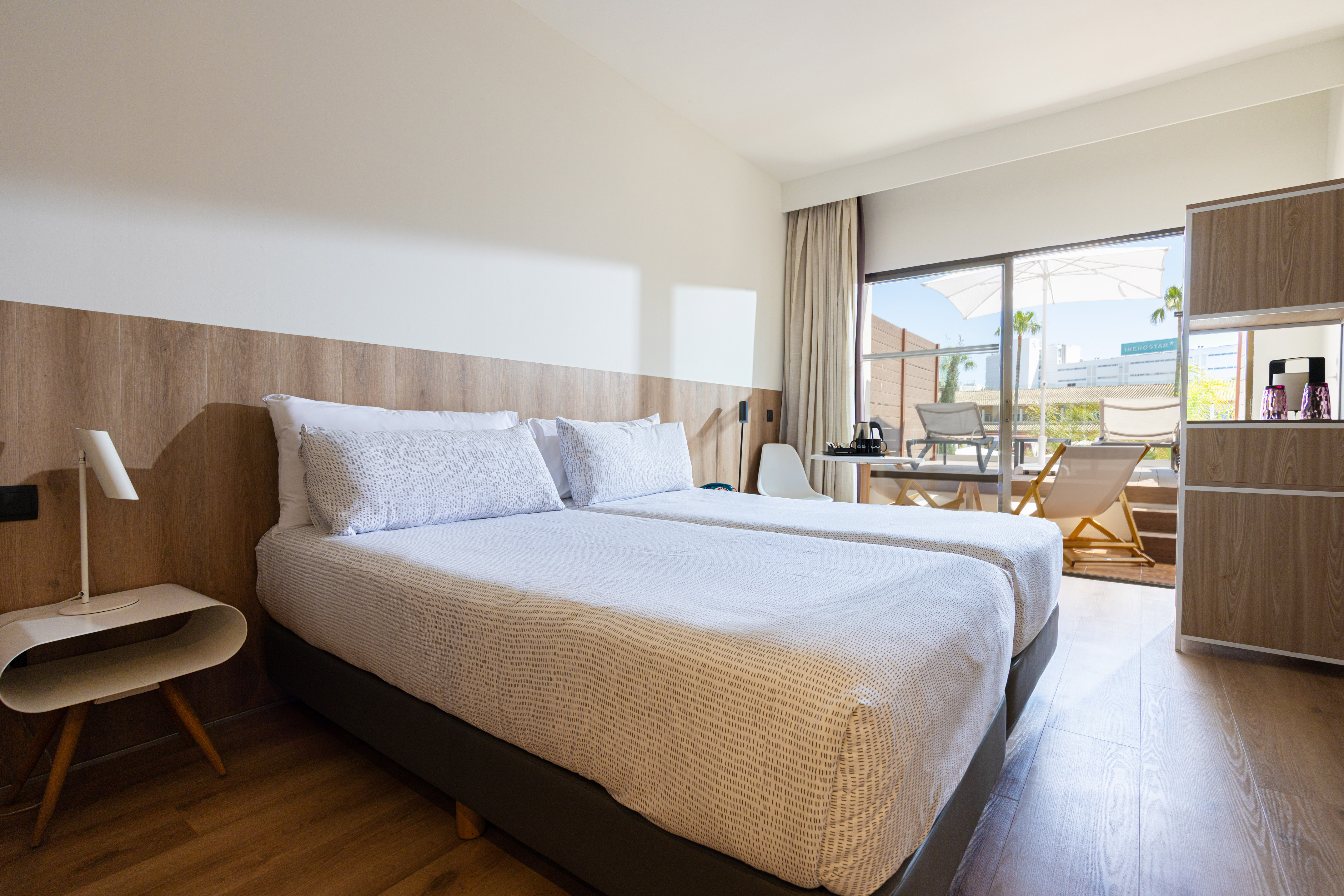 Modern hotel room with twin beds, wooden details, and a furnished balcony.