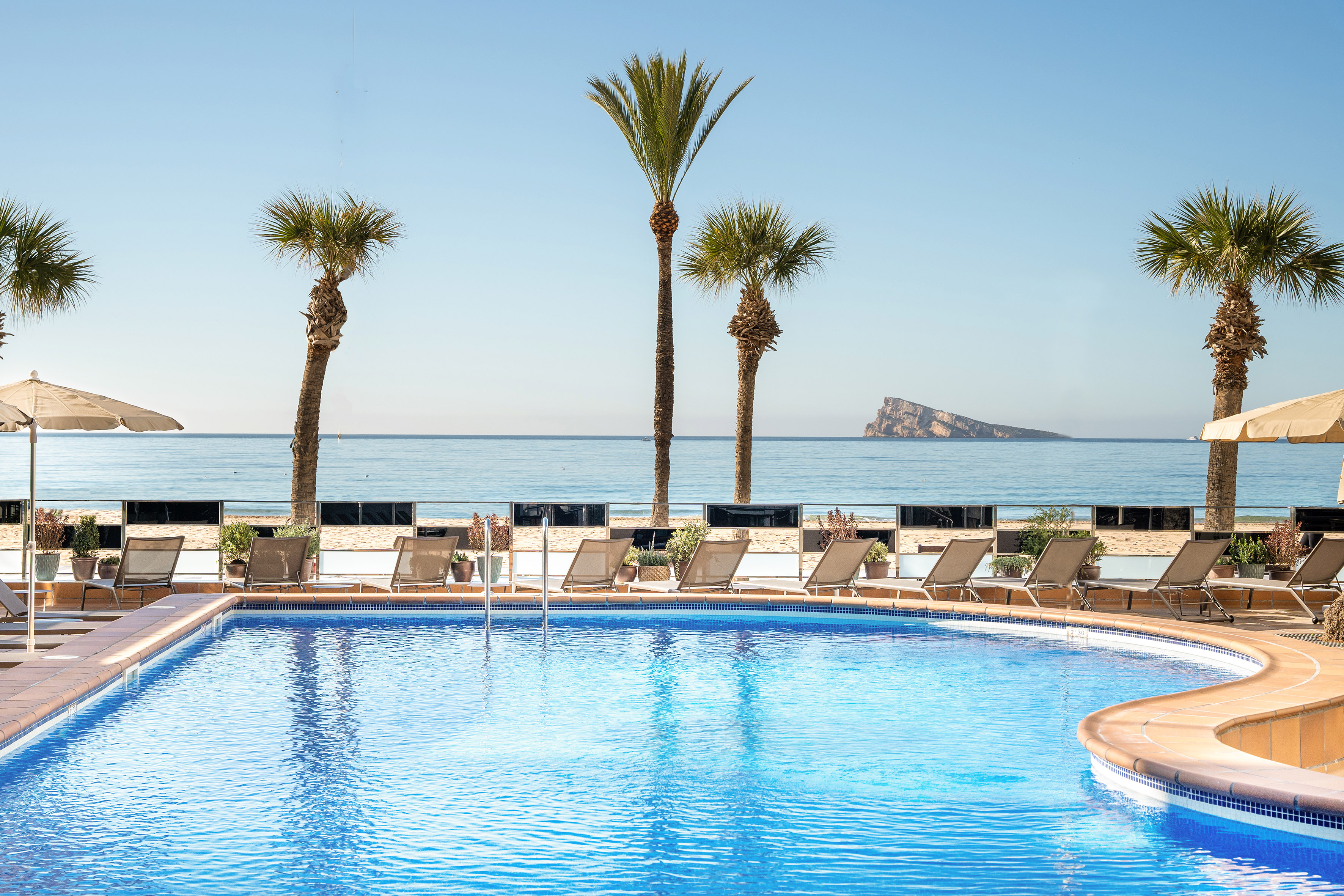 Resort swimming pool, palm trees, beach, sea, and distant island.