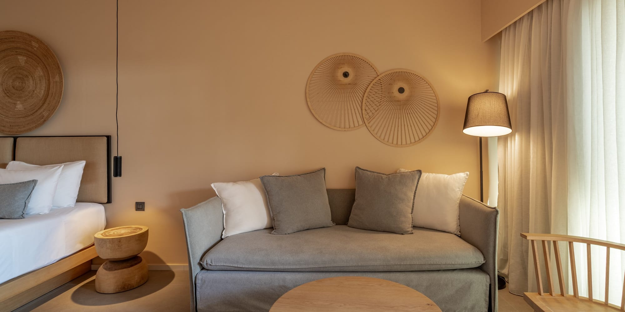 Modern hotel suite with neutral decor, grey sofa, and natural wood furniture.