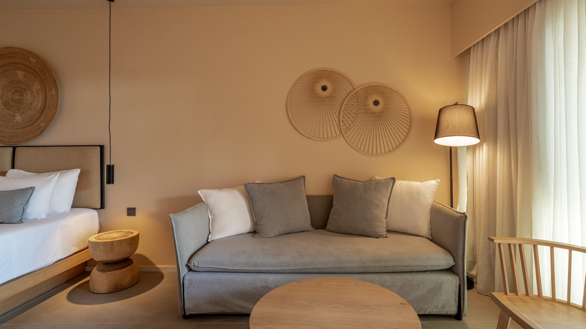 Modern hotel suite with neutral decor, grey sofa, and natural wood furniture.