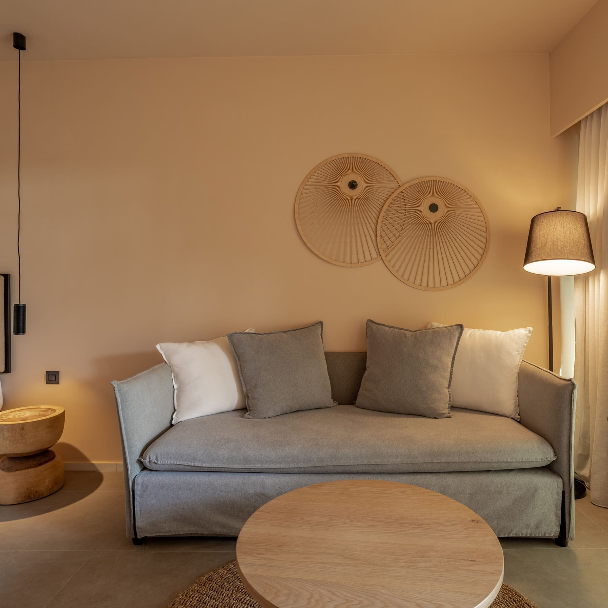 Modern hotel suite with neutral decor, grey sofa, and natural wood furniture.