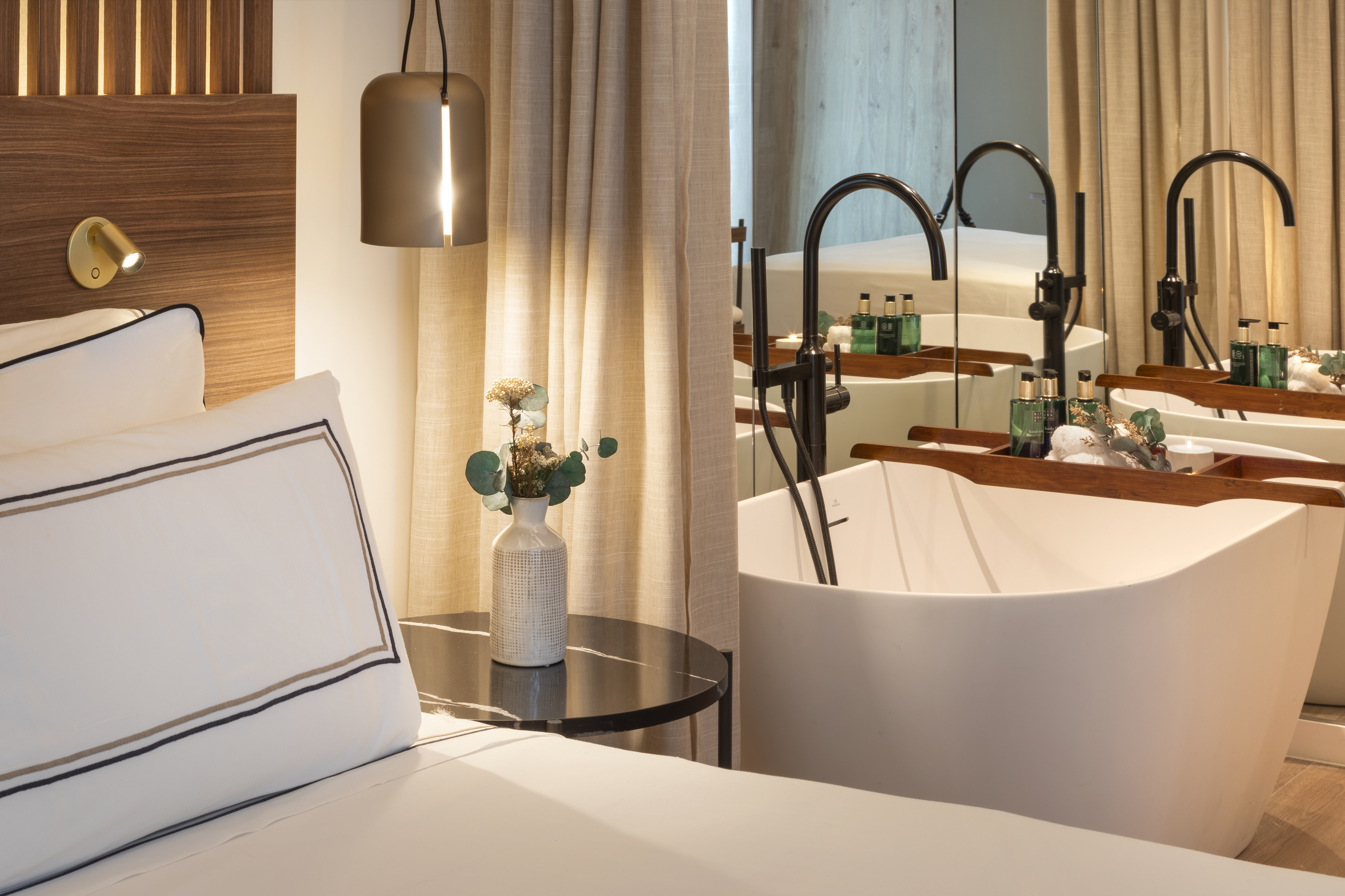 Luxury hotel bedroom with bed, elegant lighting, and modern bathtub.