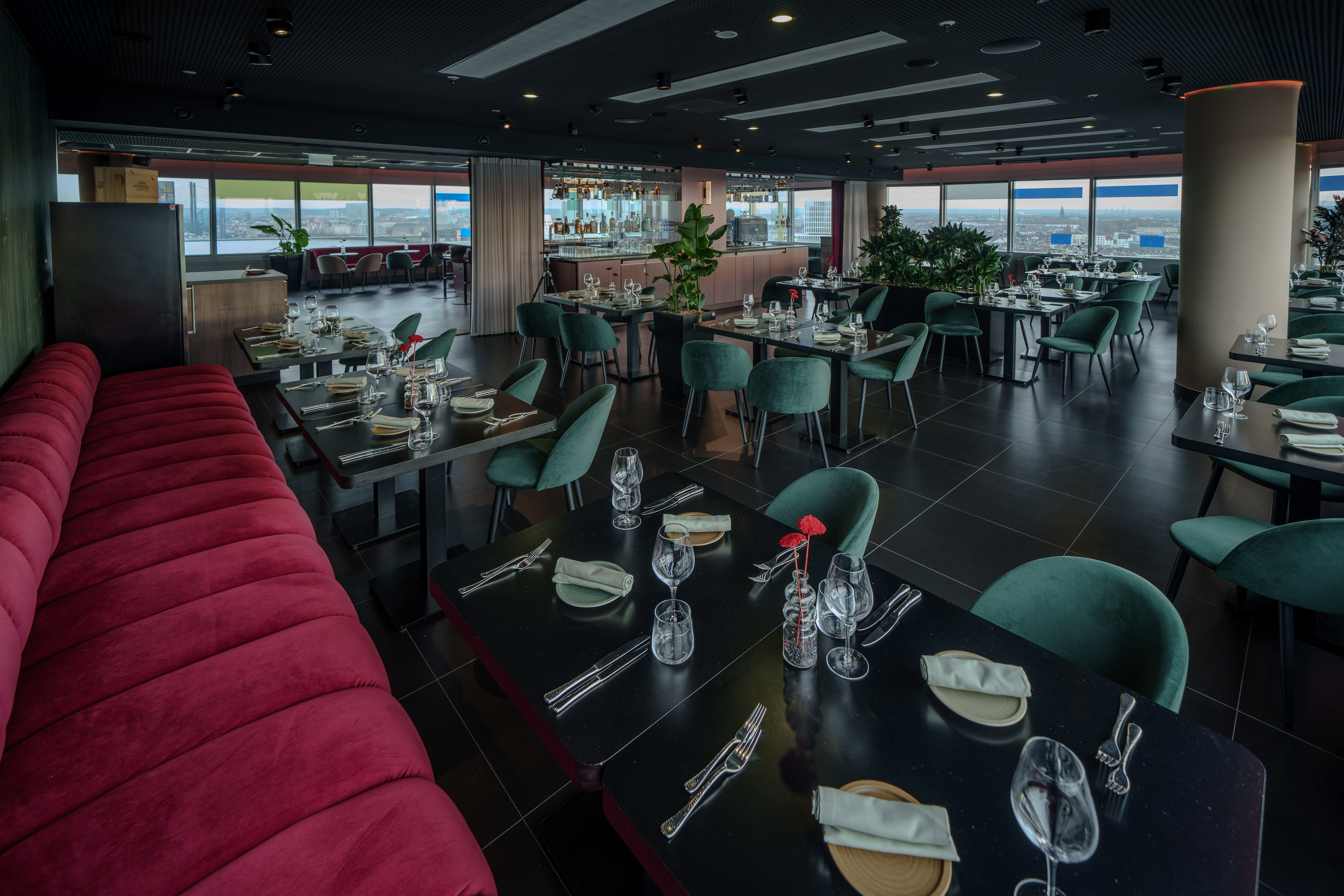 Modern restaurant interior, city view, green velvet chairs, red booth, bar.