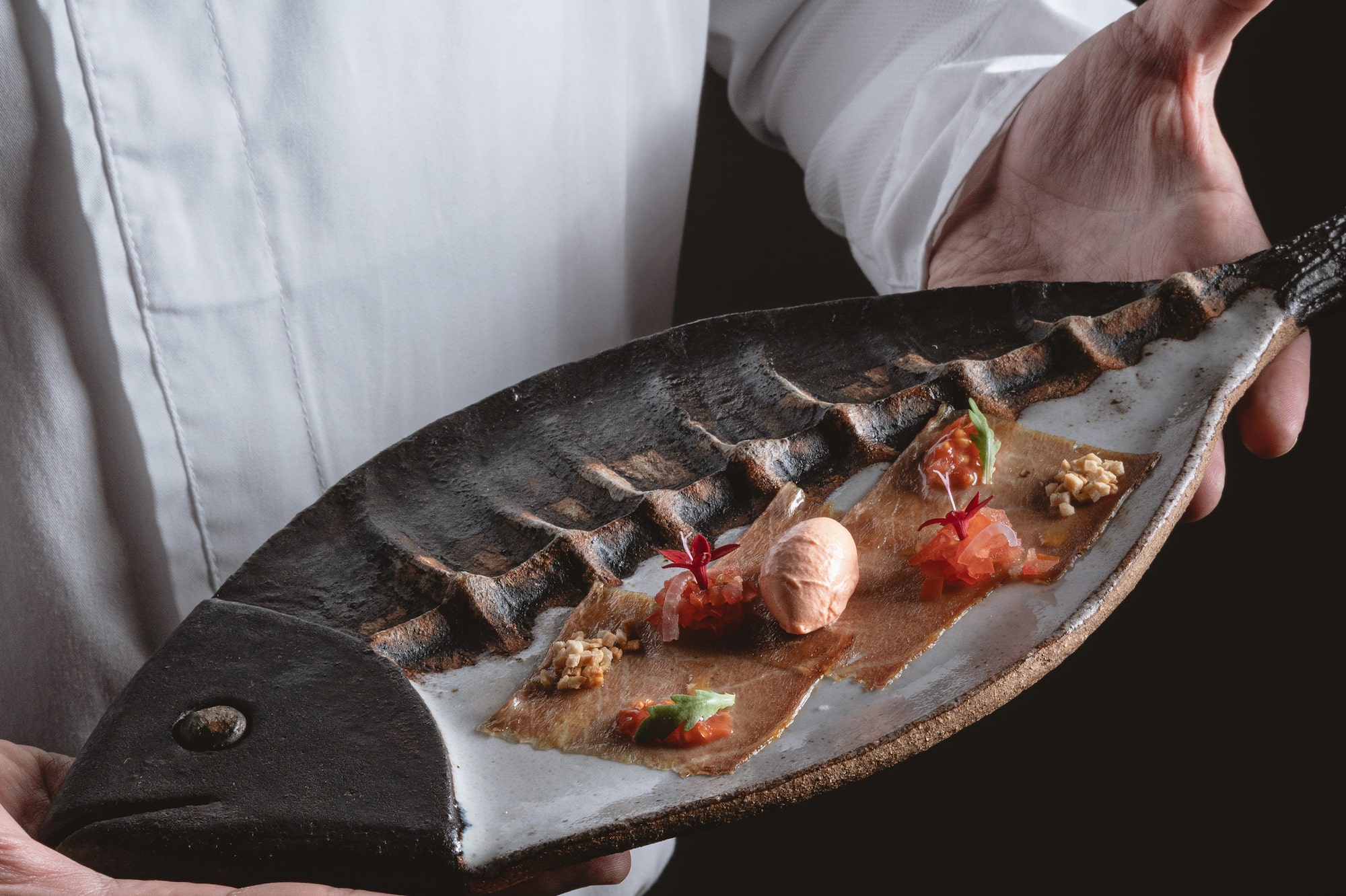 Chef presenting gourmet seafood appetizer on a fish-shaped plate.