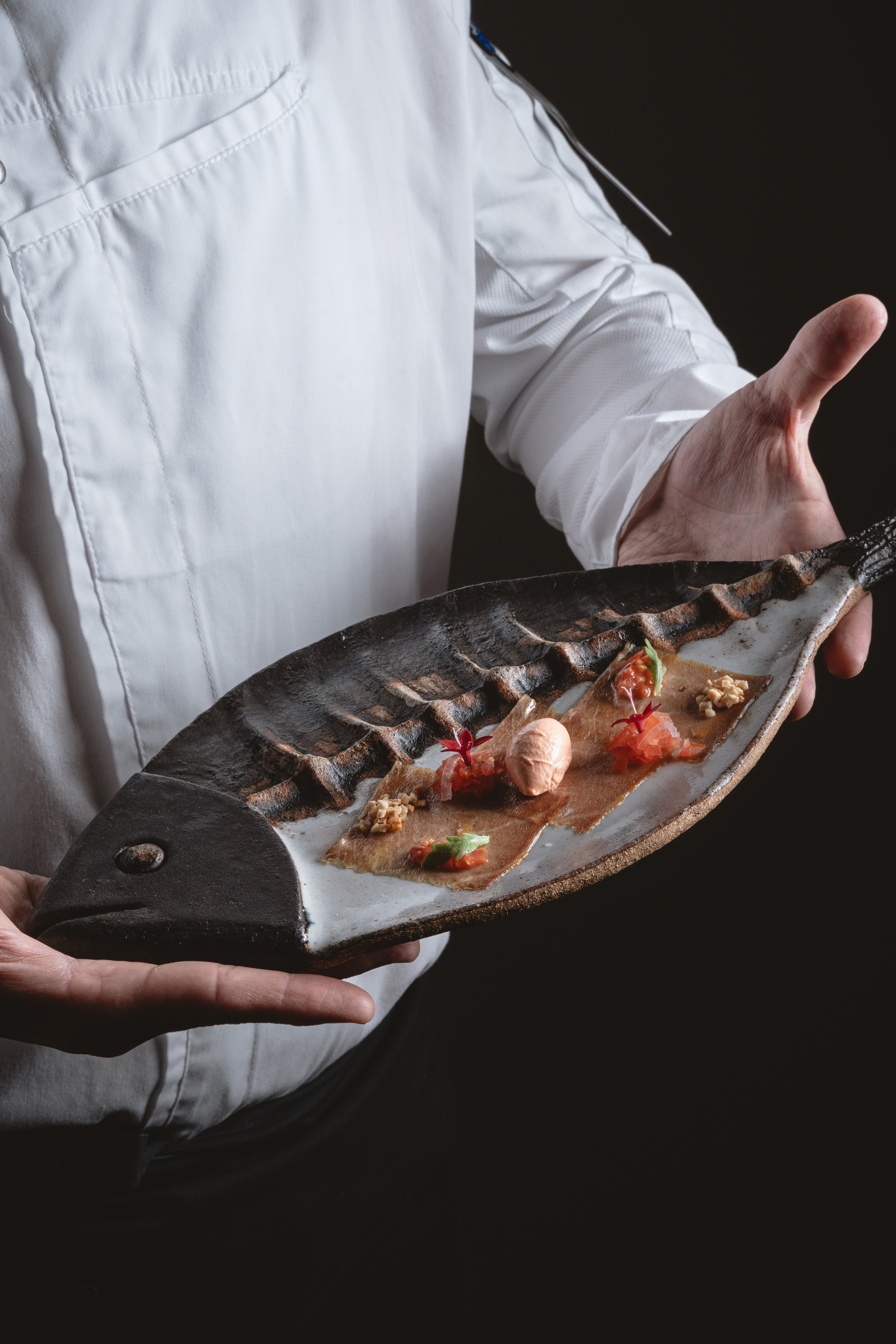 Chef presenting gourmet seafood appetizer on a fish-shaped plate.
