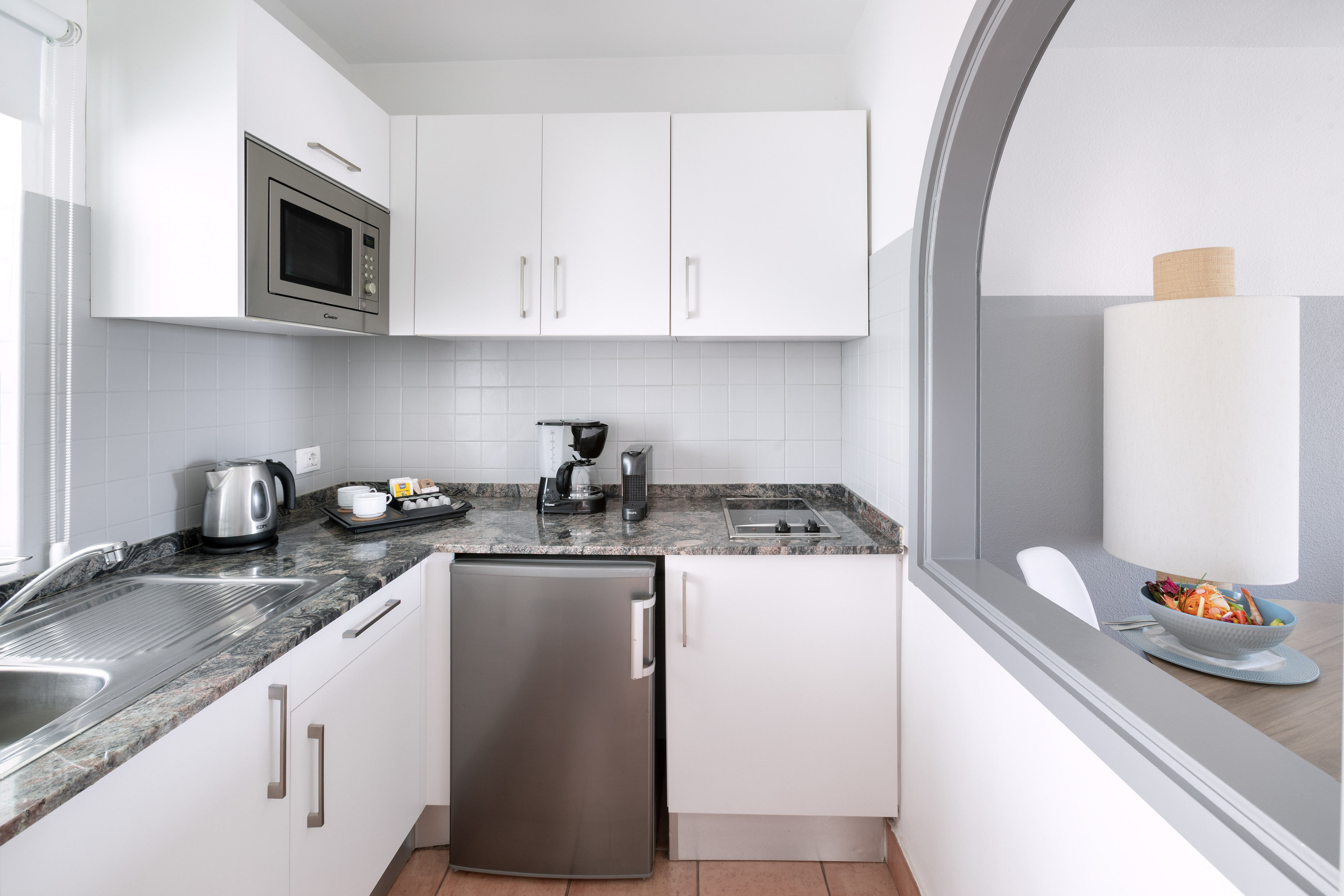 Studio apartment kitchenette with white cabinets, microwave, mini-fridge.