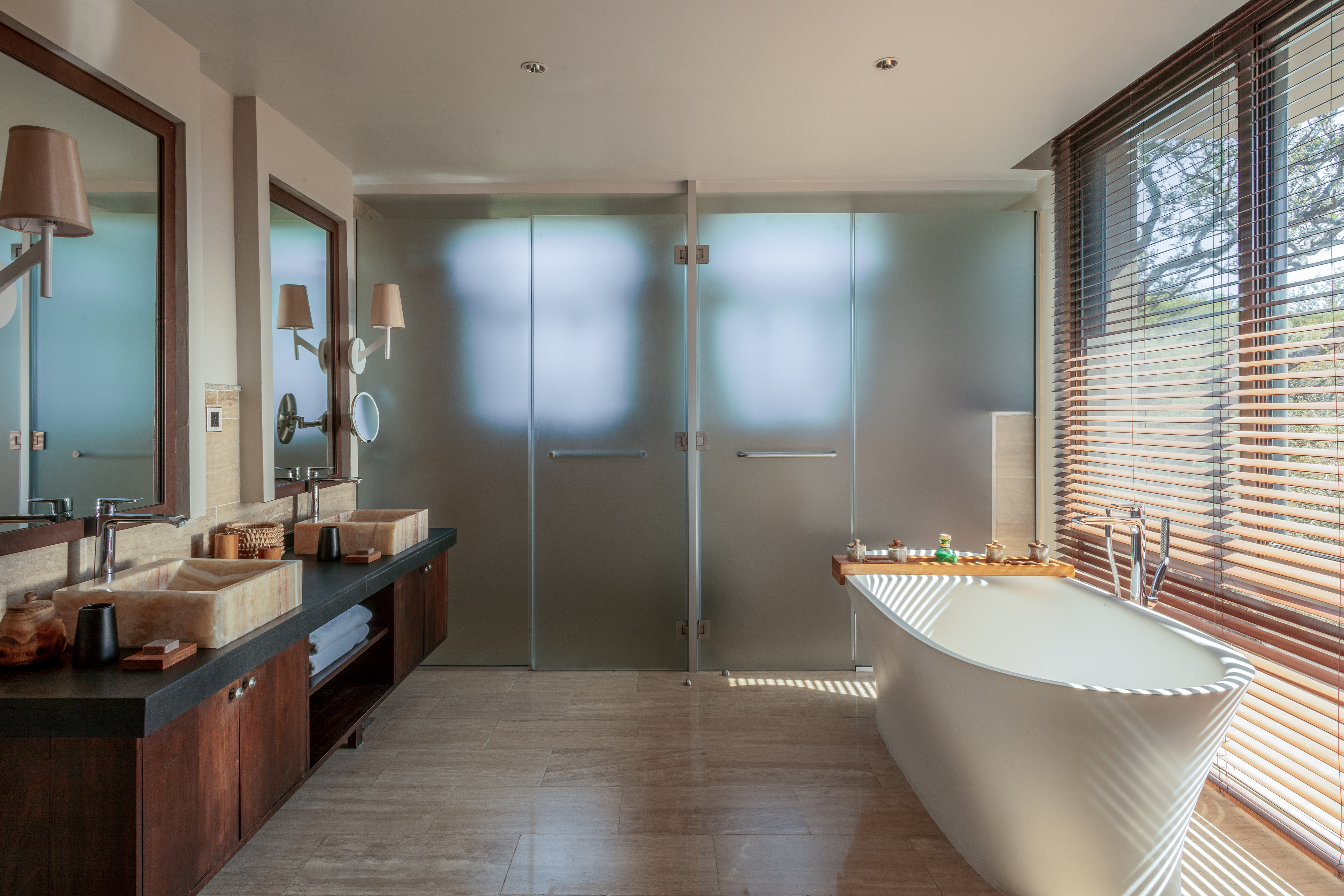 Modern bathroom with freestanding tub, double vanity, frosted shower, sunlit.