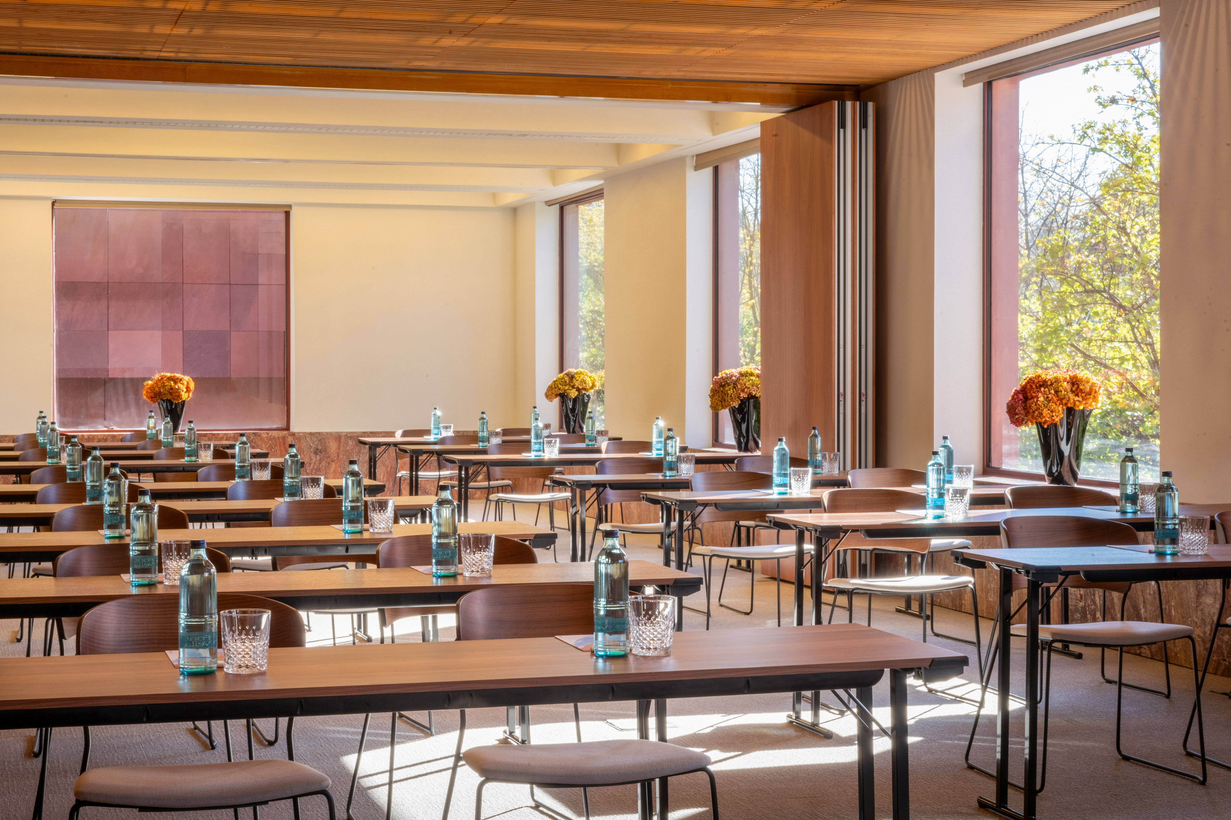 Bright conference room setup with tables, chairs, water, and large windows.