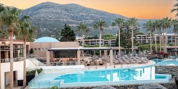 a pool with chairs and a building with mountains in the background
