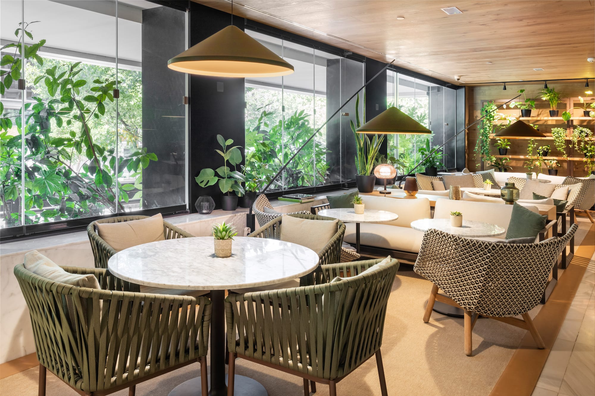 Biophilic lounge interior with green plants, comfy seating, marble tables, and large windows.