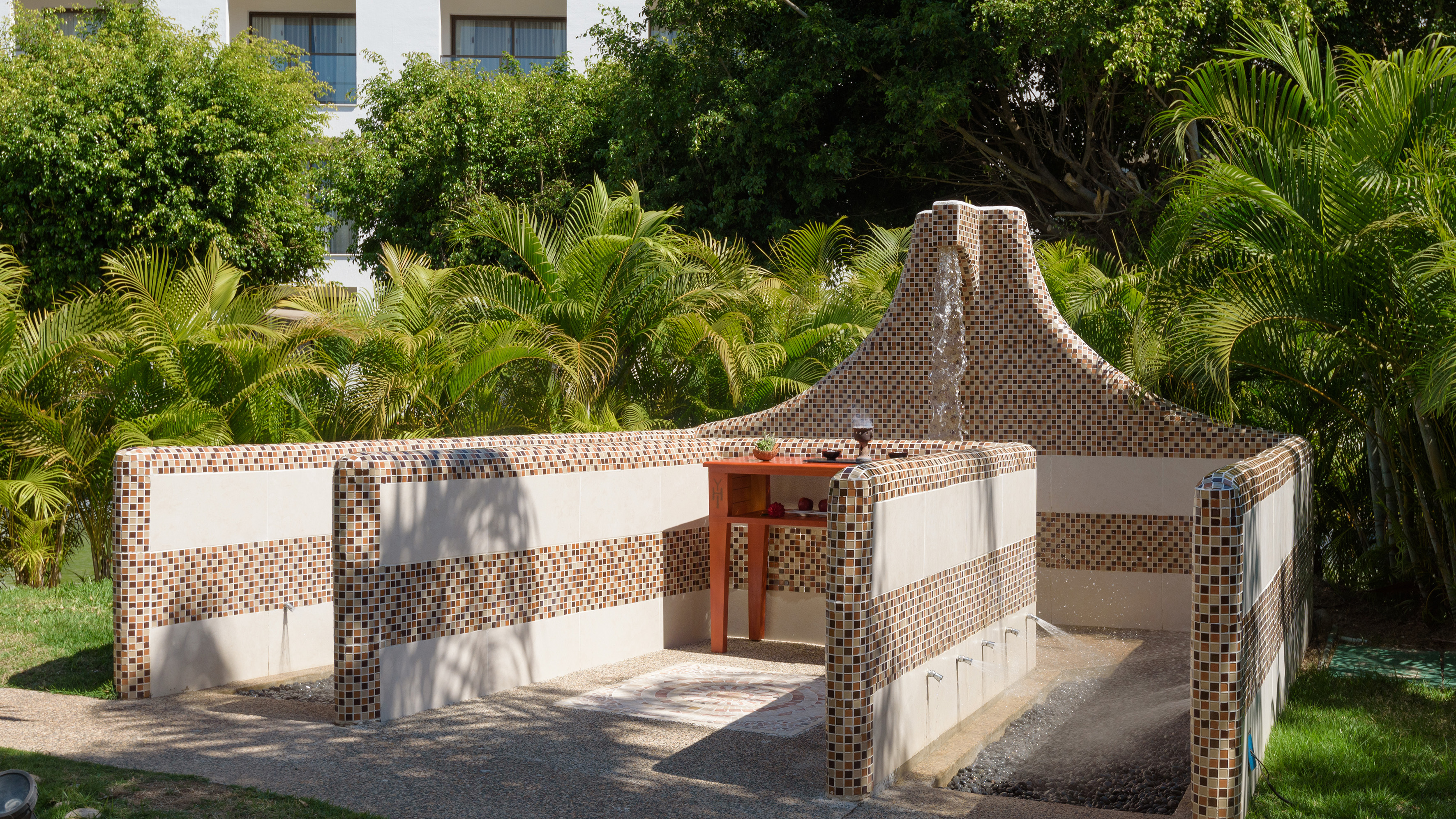 Mosaic tiled outdoor shower with waterfall, wall jets, and tropical garden.