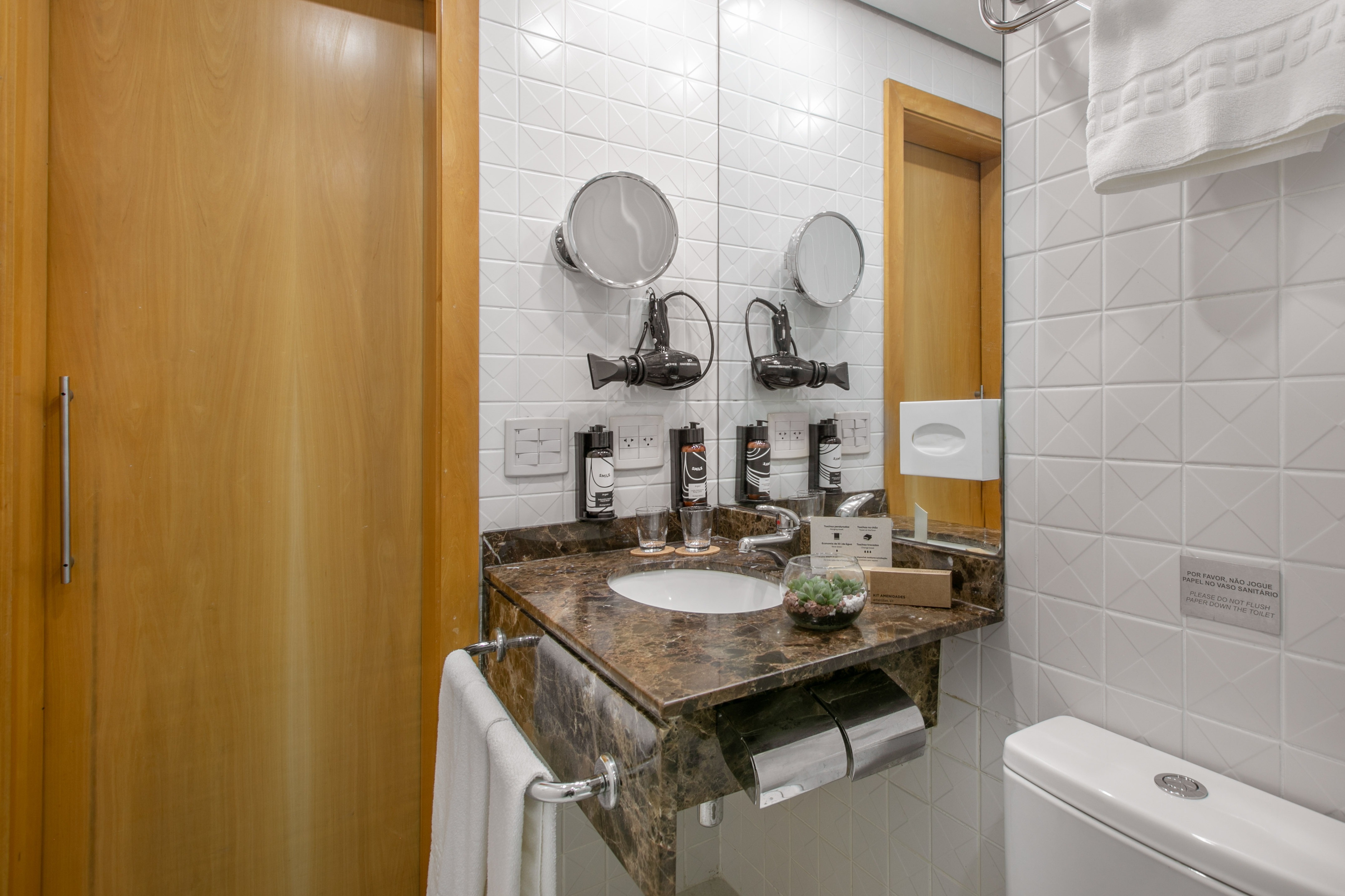 Modern hotel bathroom with marble vanity, sink, mirror, and white tiles.