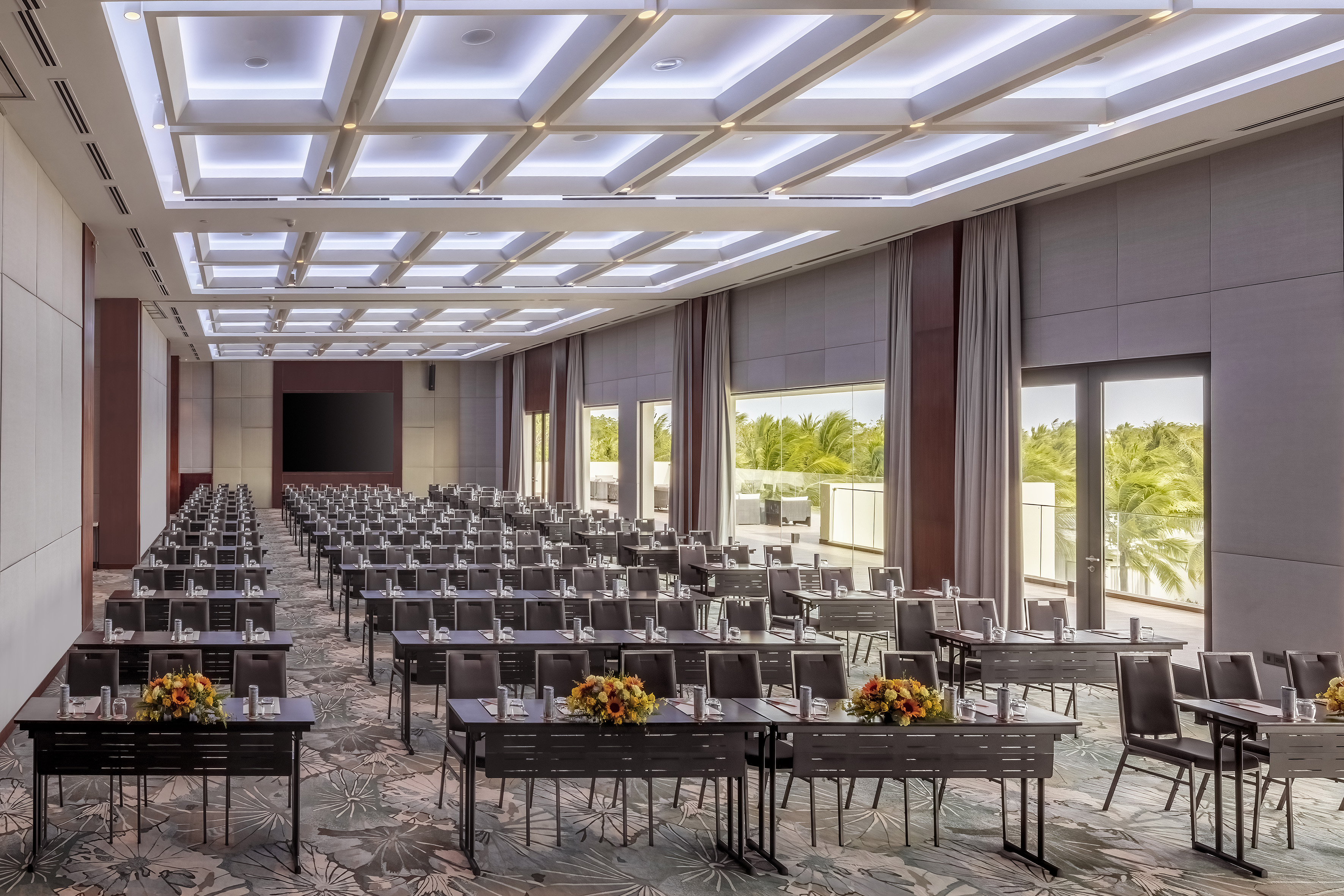 Modern conference room with classroom setup, large screen, tropical view.