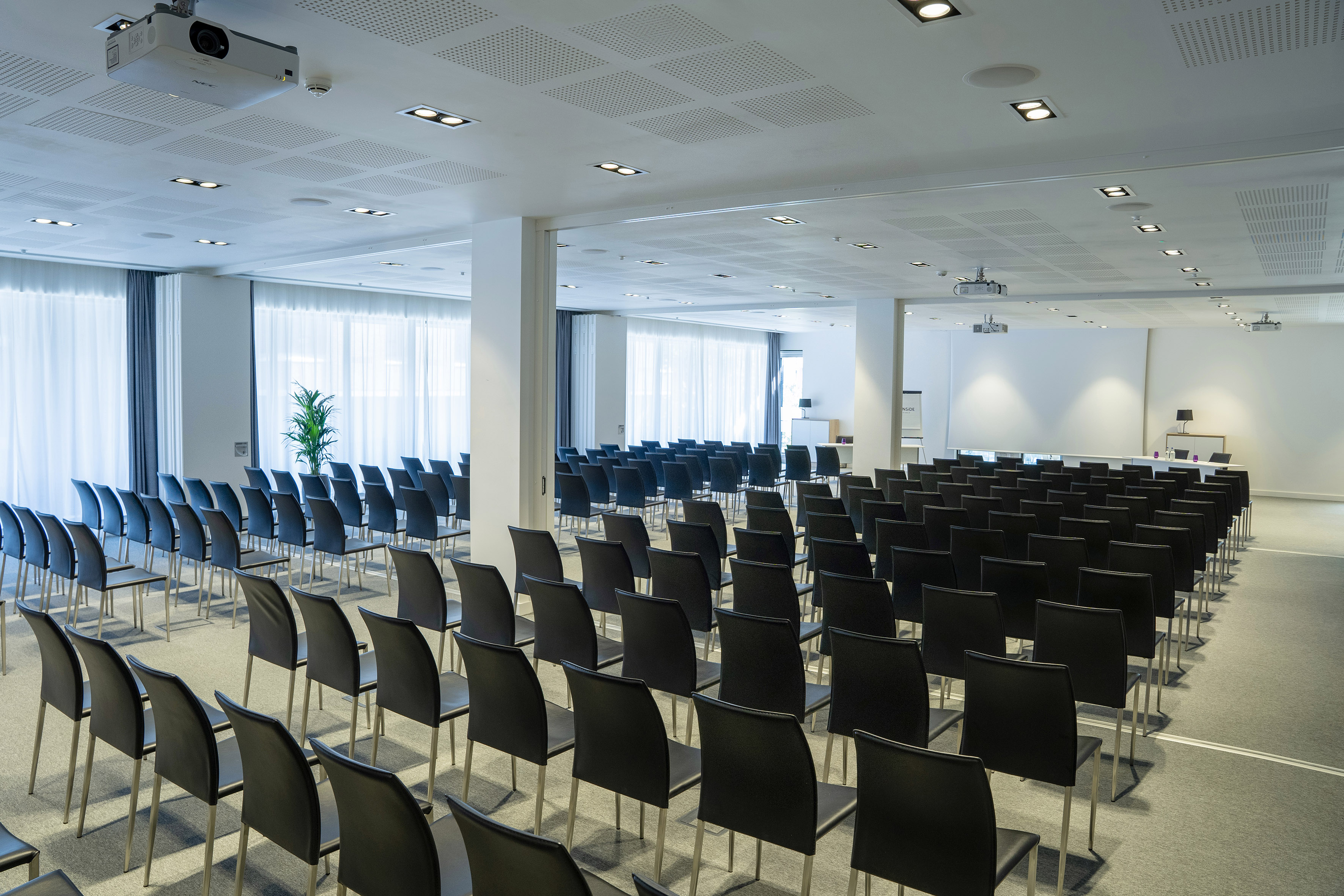 Empty modern conference room with rows of black chairs, projector, and screen.