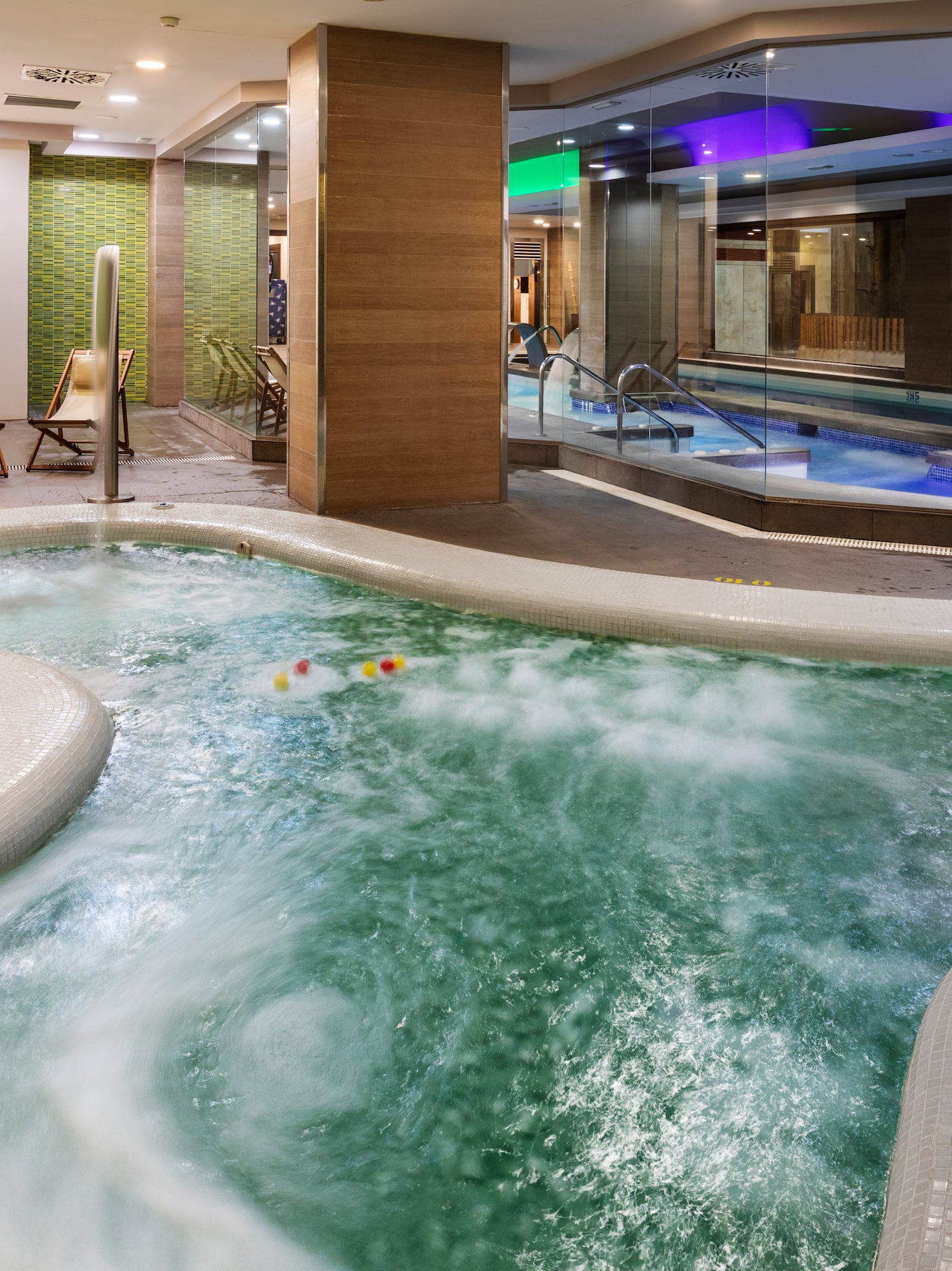 Bubbling indoor jacuzzi at a modern spa with an adjacent swimming pool.