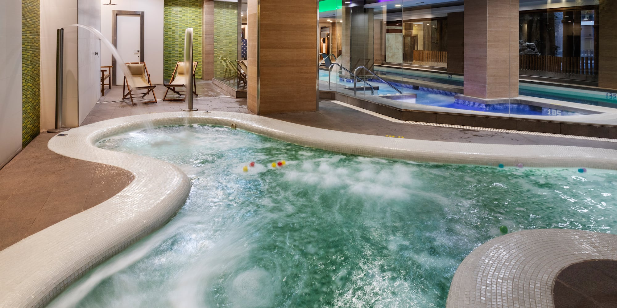 Relaxing indoor spa with large bubbling jacuzzi and adjacent swimming pool.
