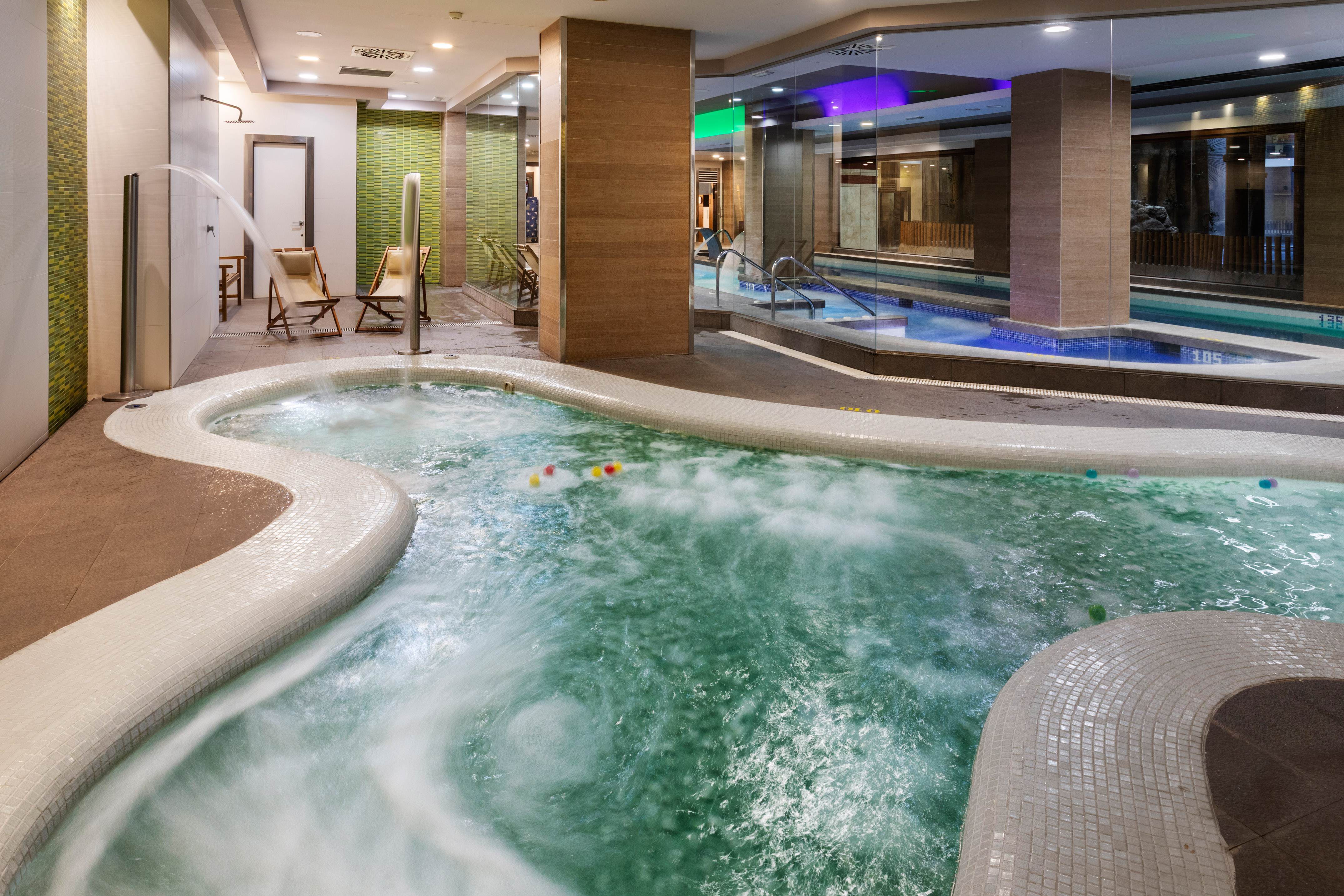 Bubbling indoor jacuzzi at a modern spa with an adjacent swimming pool.