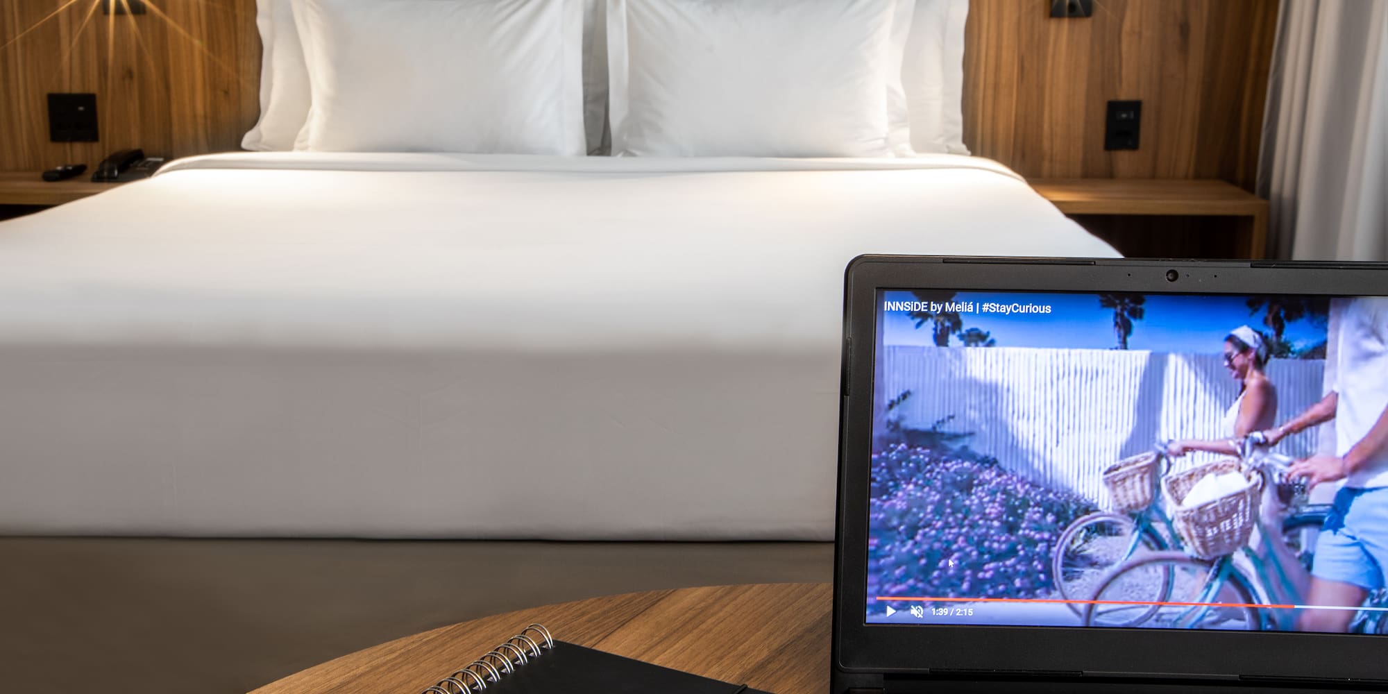 a laptop and a pen on a table in front of a bed