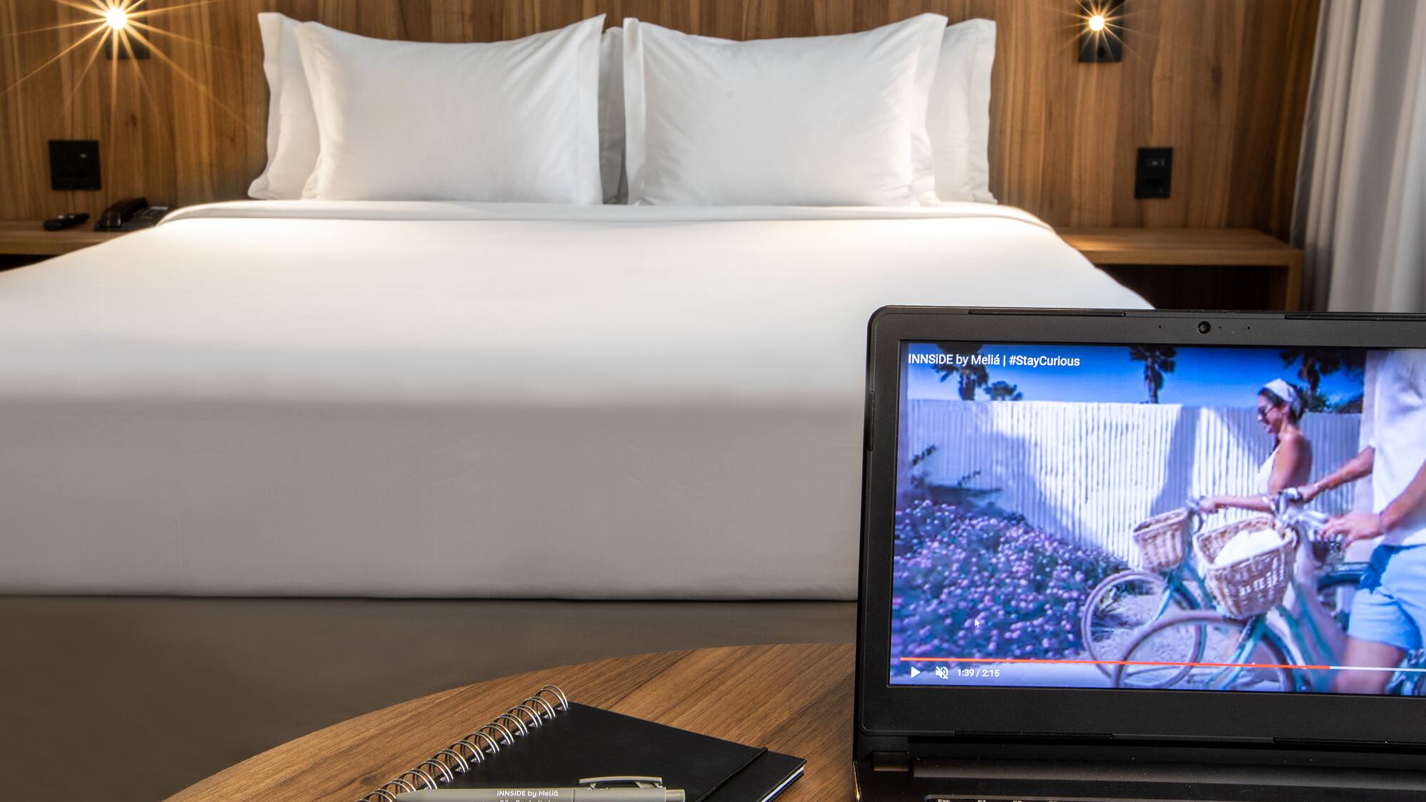 a laptop and a pen on a table in front of a bed