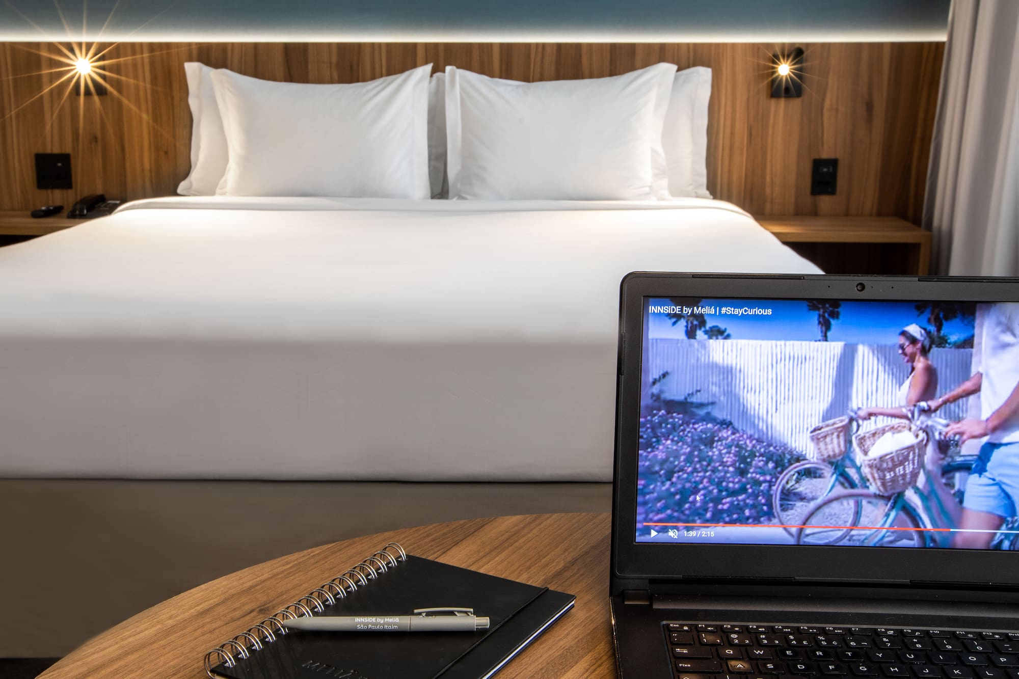 a laptop and a pen on a table in front of a bed