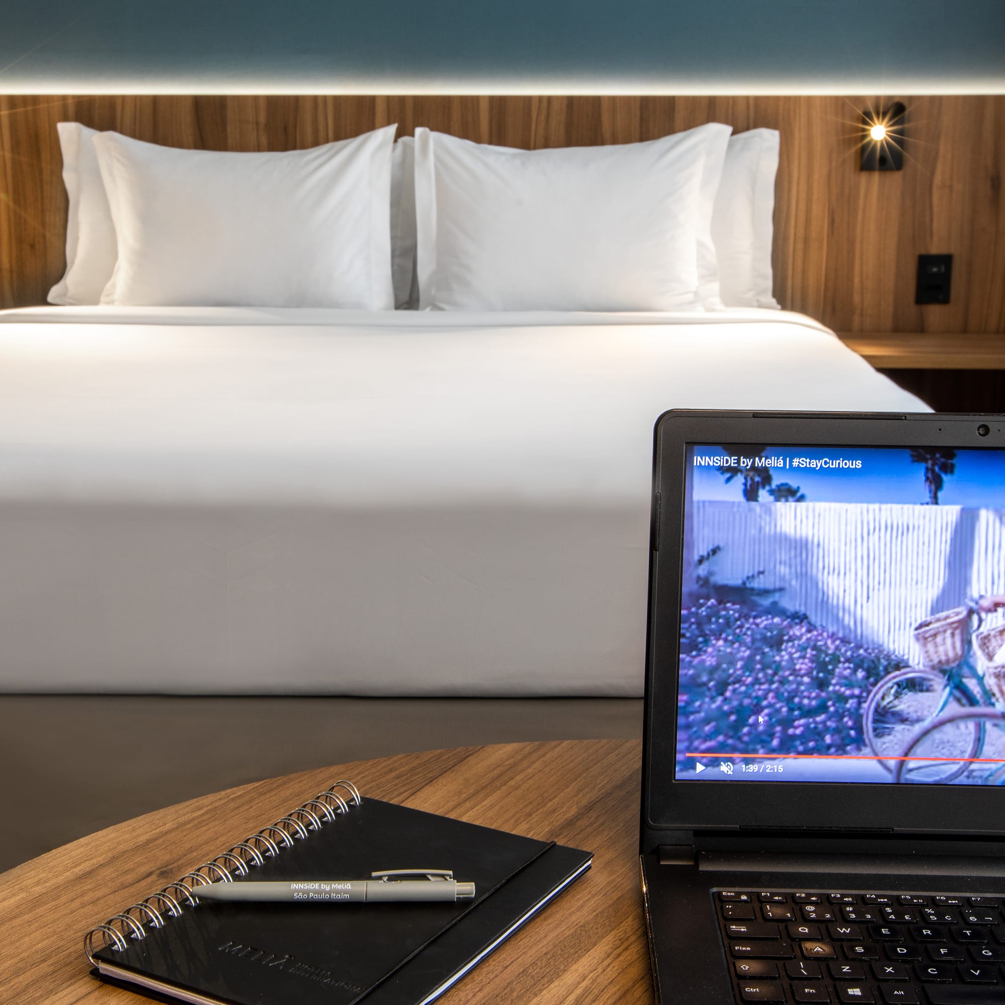 a laptop and a pen on a table in front of a bed