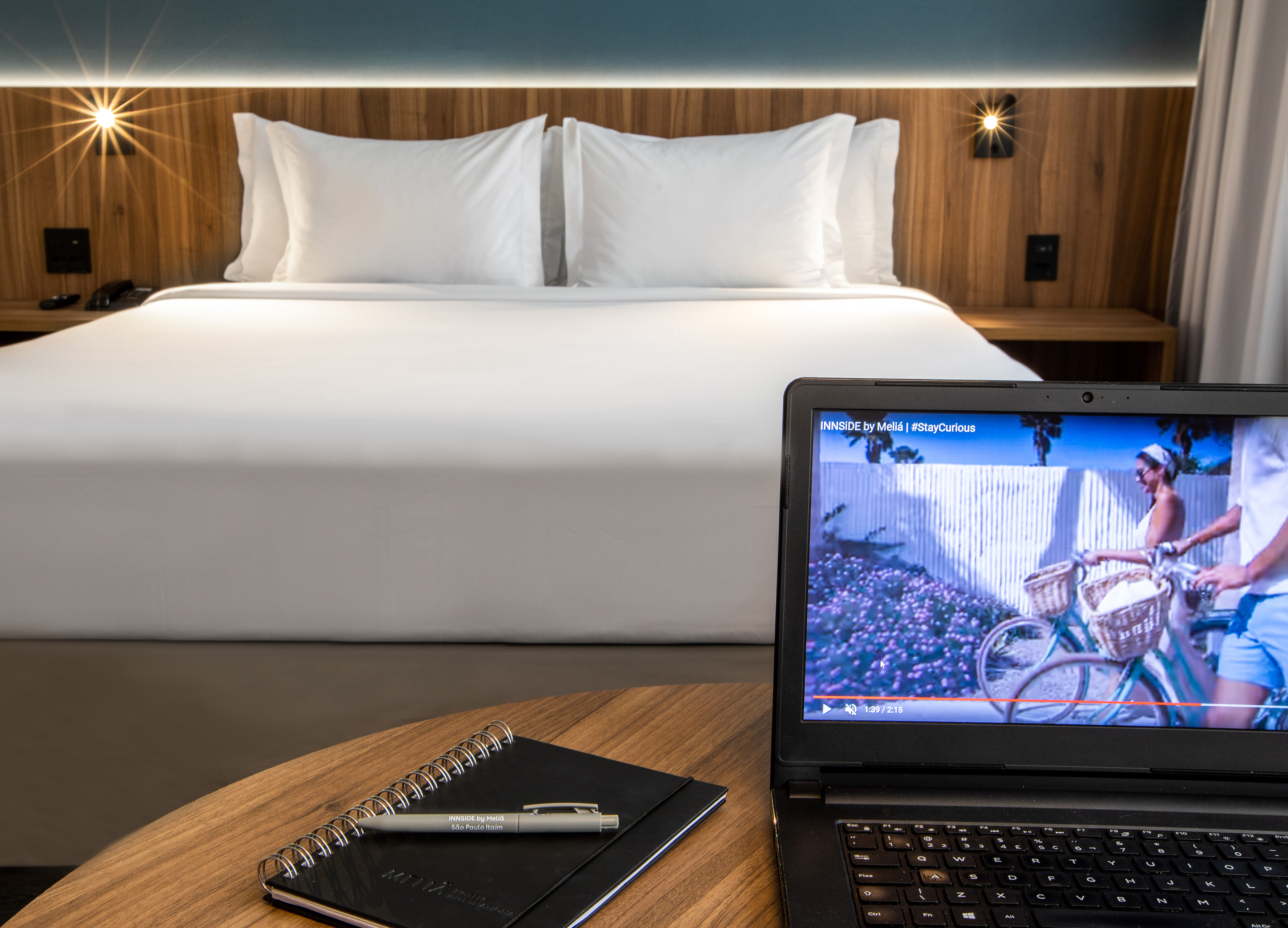 a laptop and a pen on a table in front of a bed