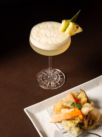 a glass of drink with a pineapple garnish on top of a plate of food