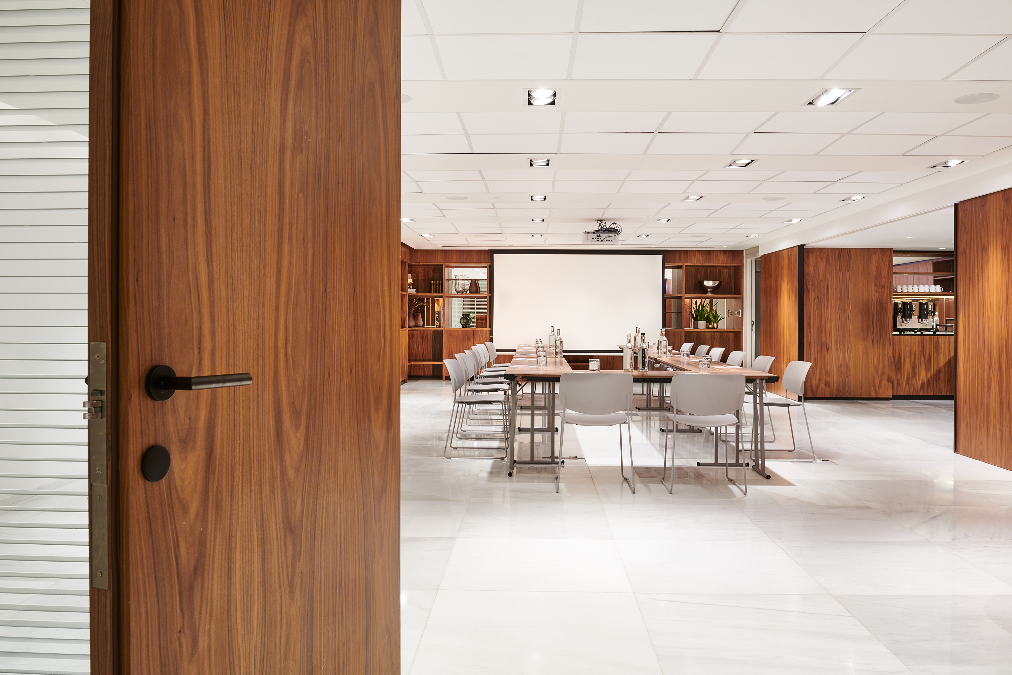 Modern conference room with wooden door, long table, and projector screen.