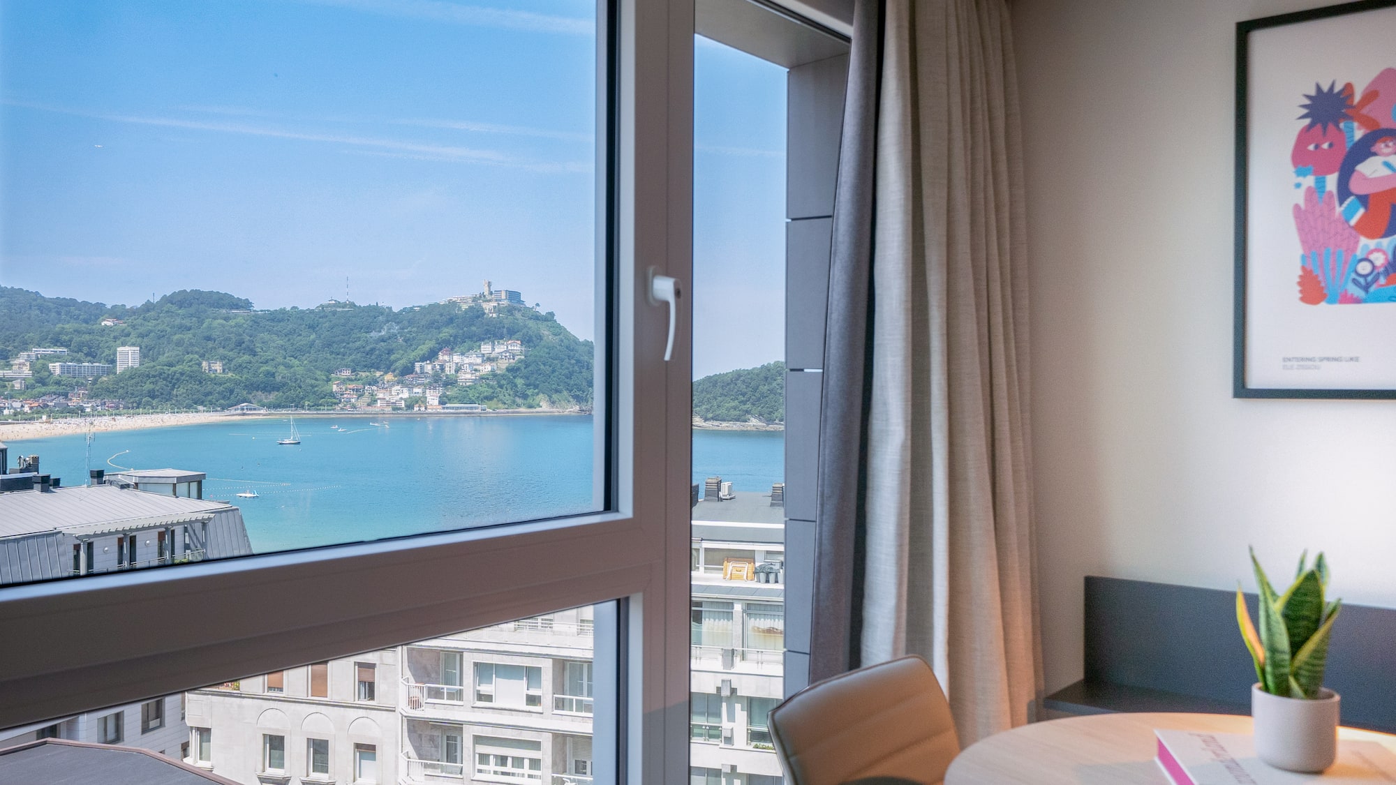 Vista desde ventana a la Bahía de La Concha, San Sebastián, con playa y montañas.