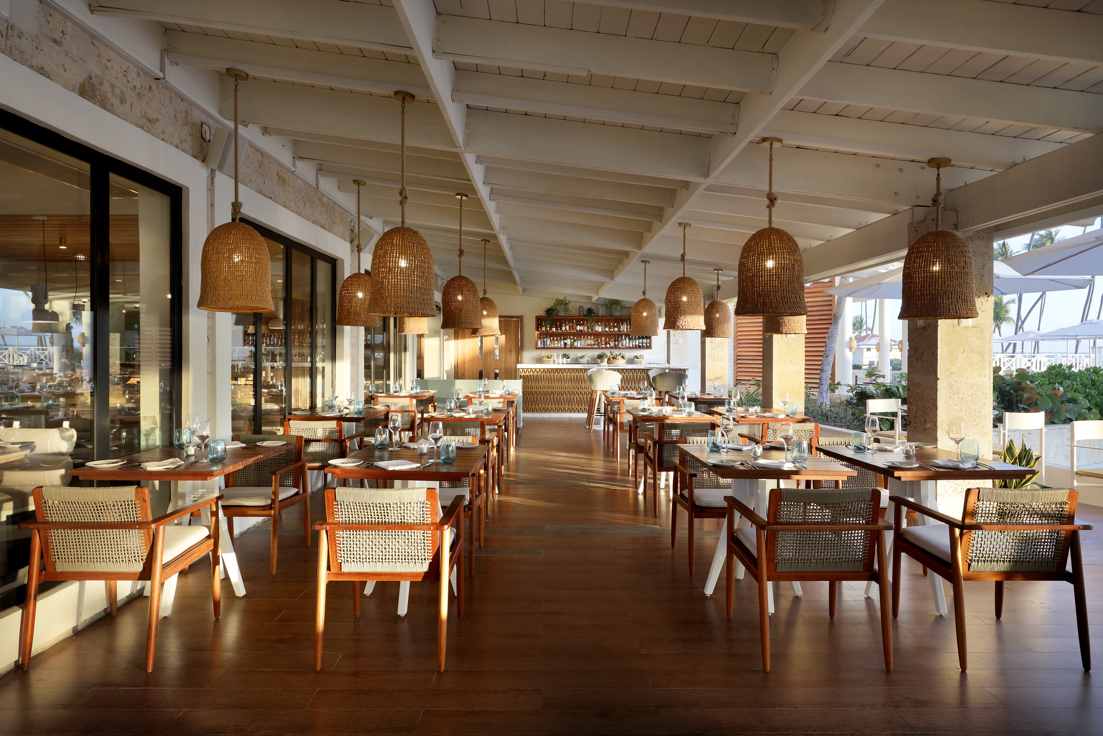 Modern resort dining area with wicker pendant lights, wooden tables, and bar.