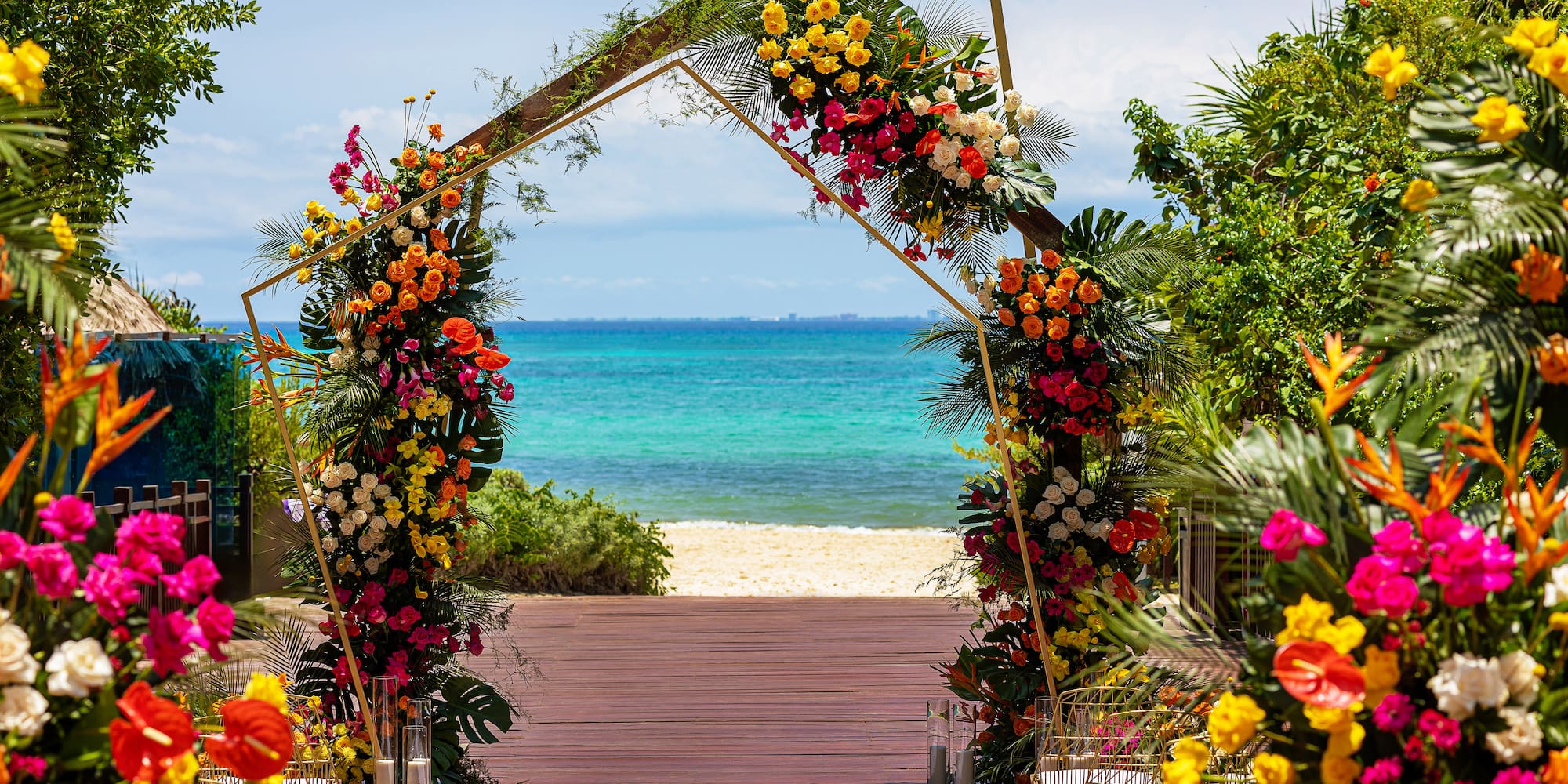 Golden arch with vibrant tropical flowers for a beach wedding ceremony, ocean view.