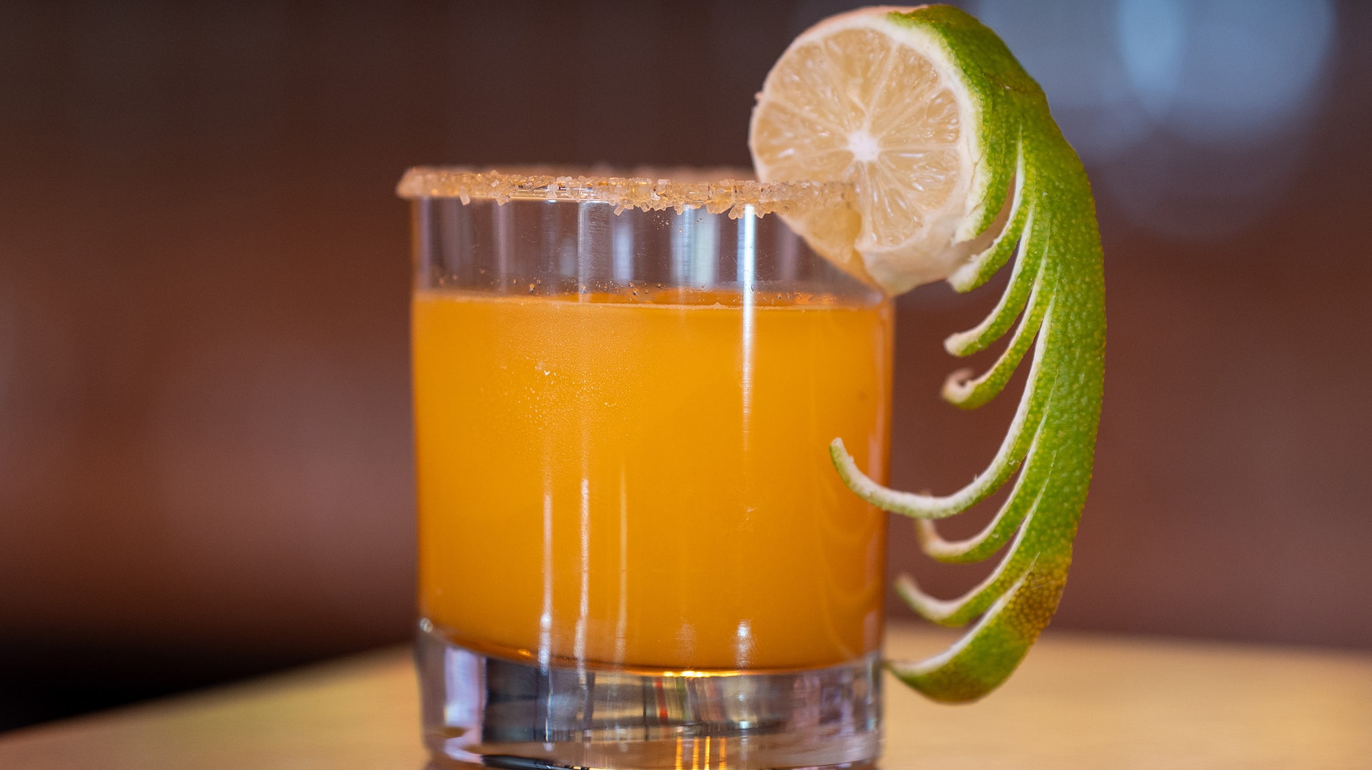 a glass of orange liquid with a lime wedge on a counter