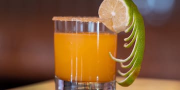 a glass of orange liquid with a lime wedge on a counter