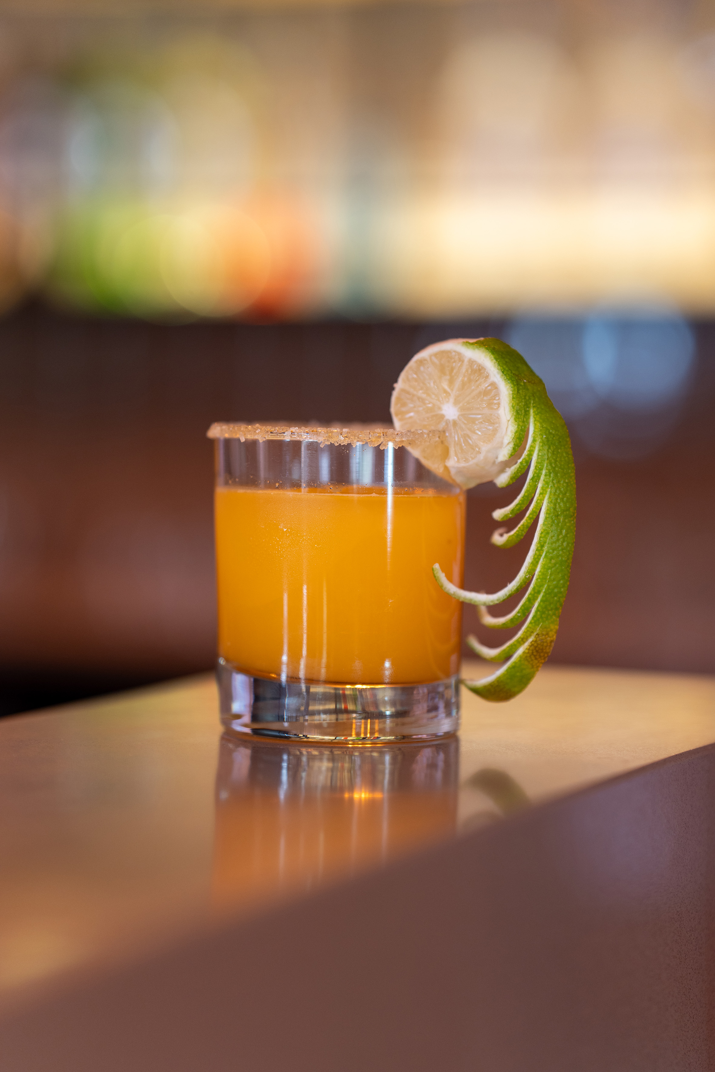 Orange cocktail in a sugar-rimmed glass with a lime garnish on a bar.