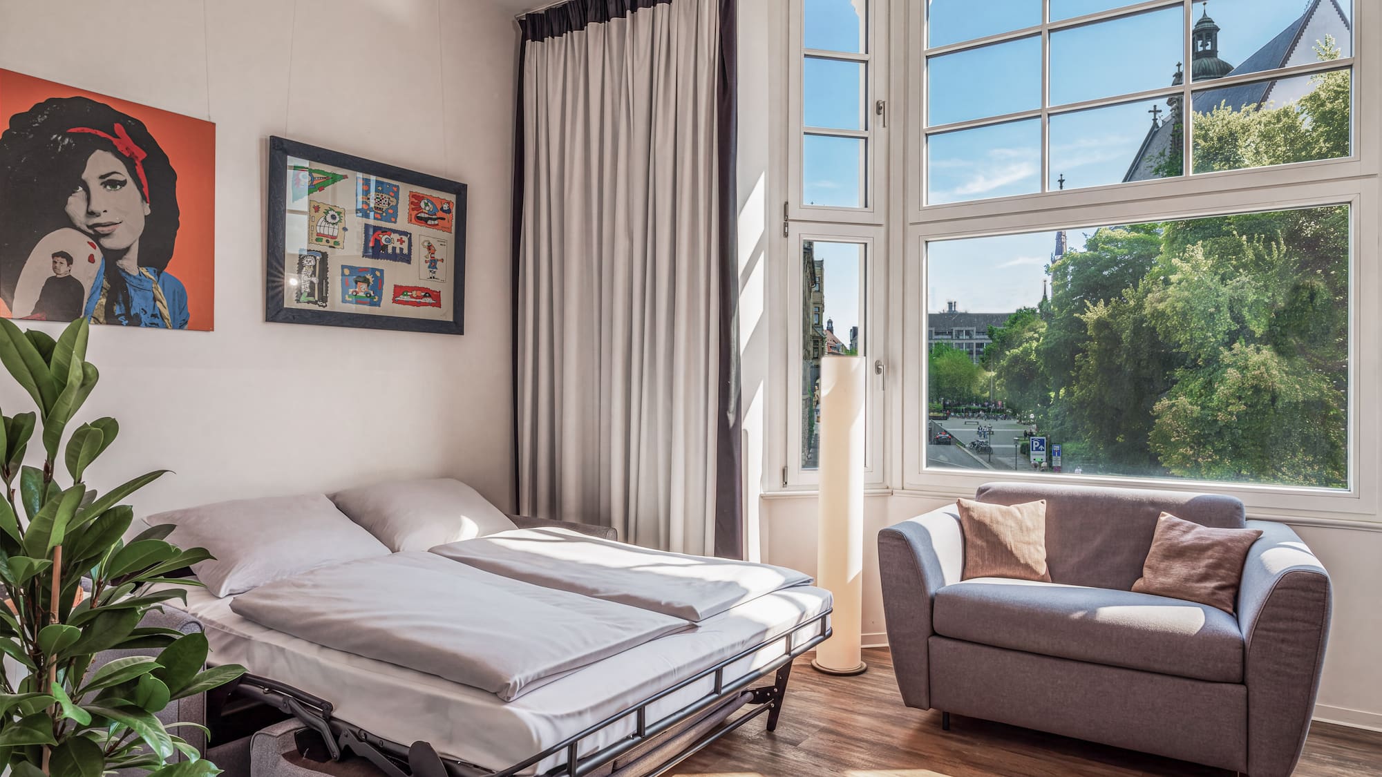 Modern studio with sofa bed, gray couch, and city view window.