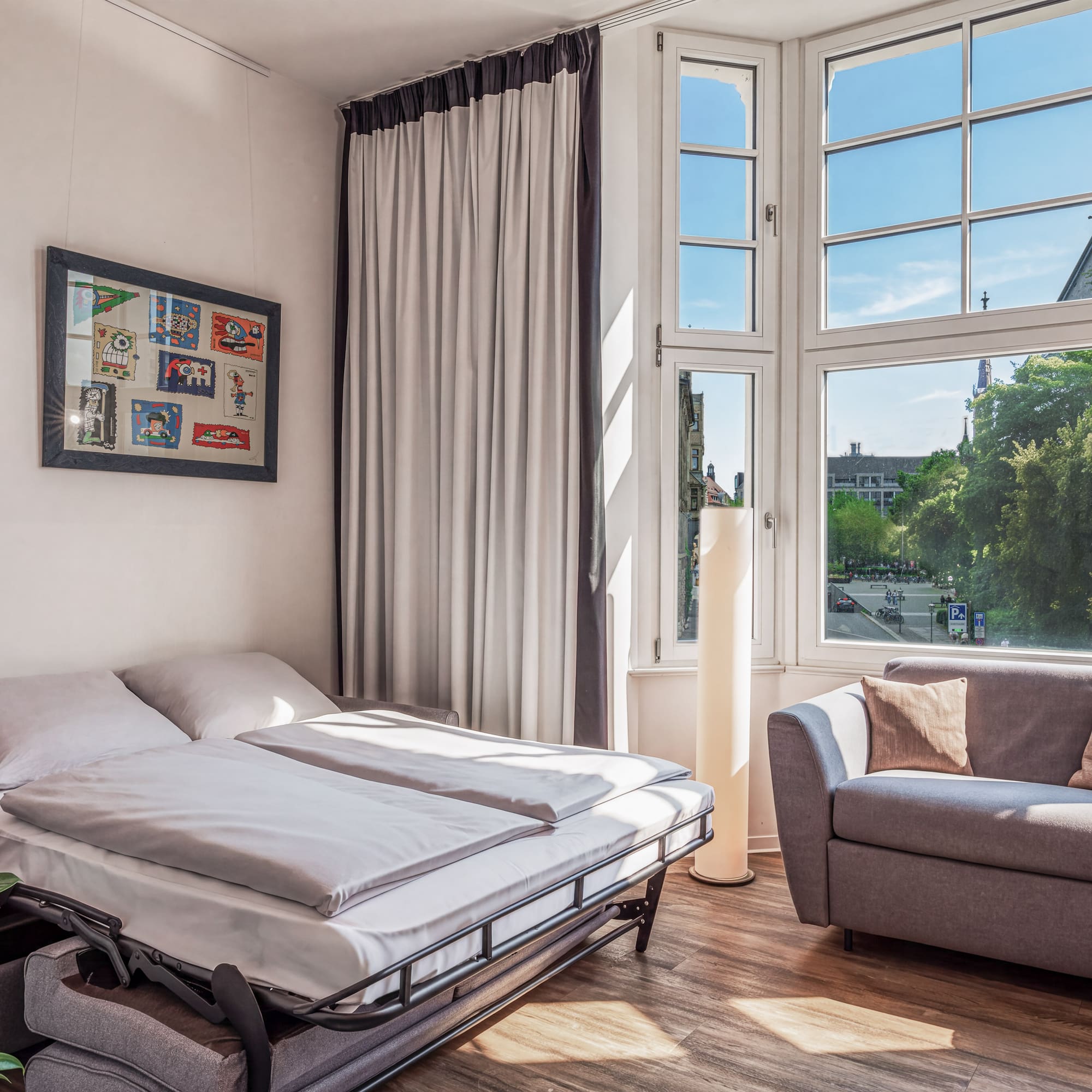 Modern studio with sofa bed, gray couch, and city view window.
